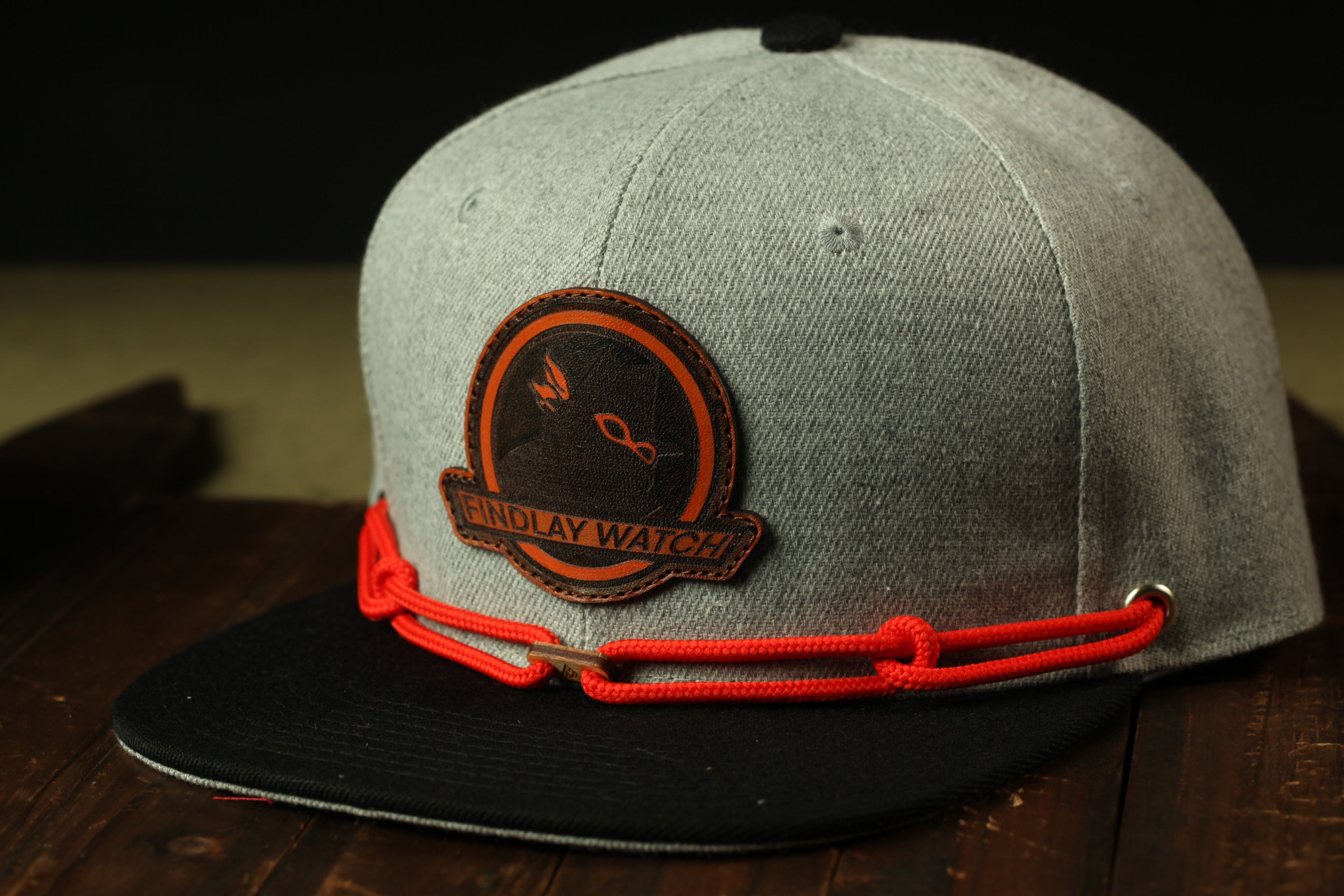 A gray baseball cap with a red string and a circular patch on the front, featuring a logo.