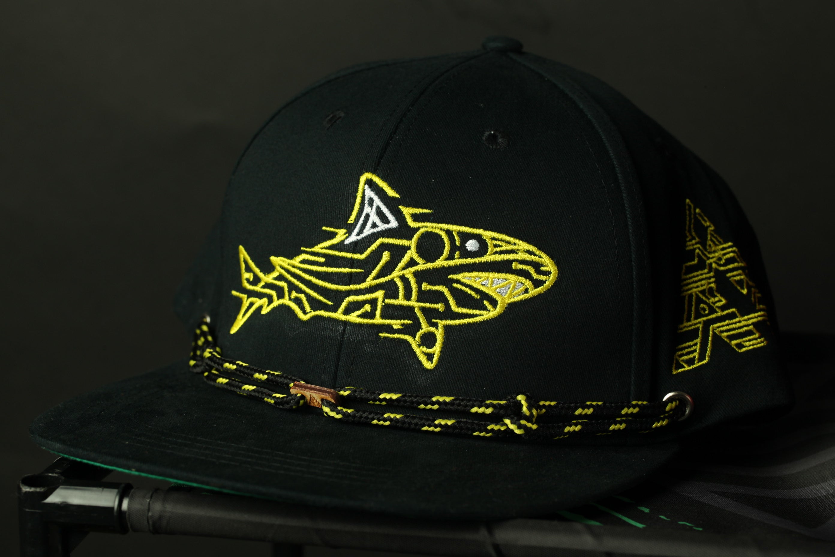 A black baseball cap with a yellow shark design on it.