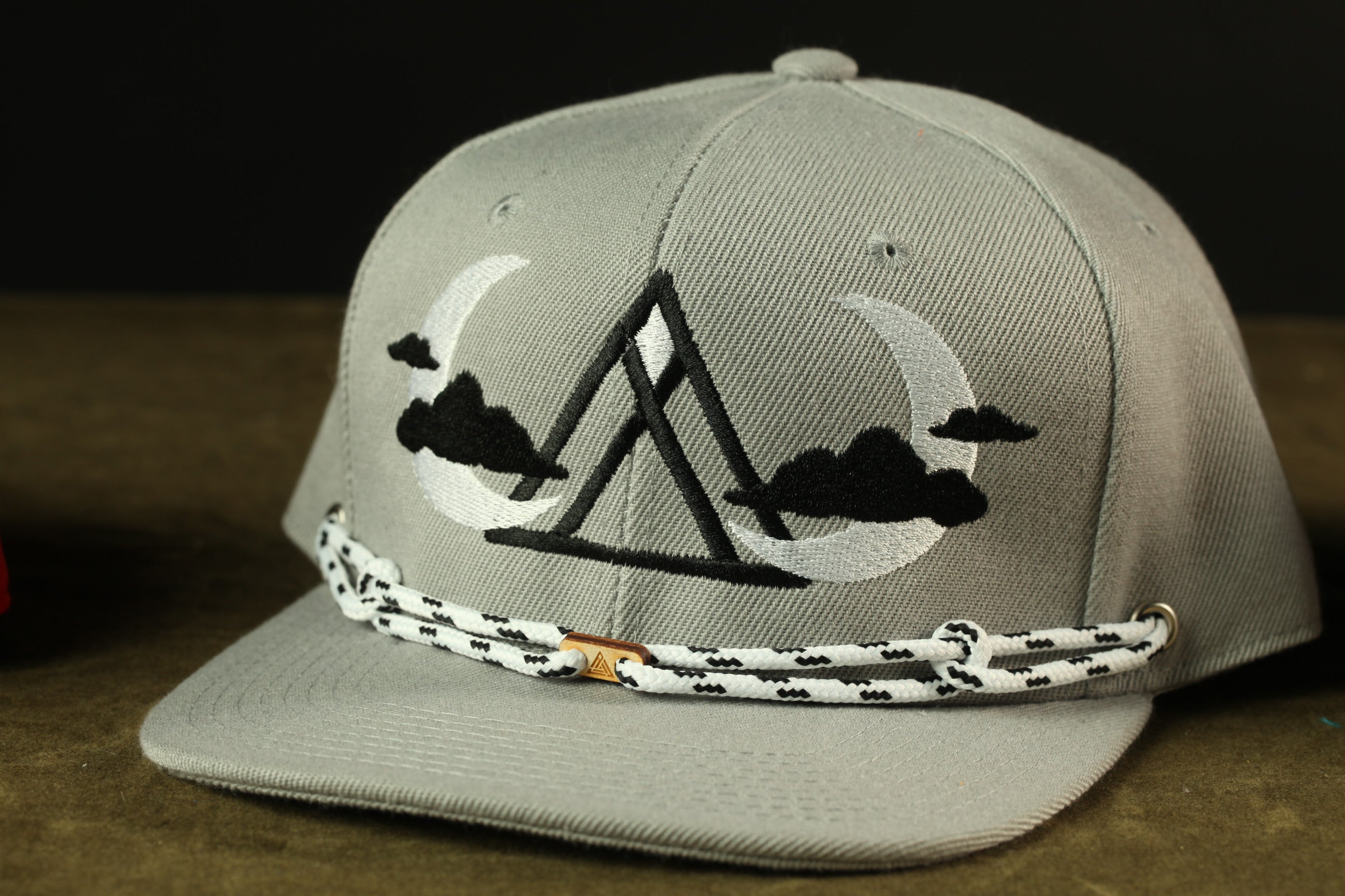 A gray baseball cap with a black and white design featuring a mountain and clouds on the front.