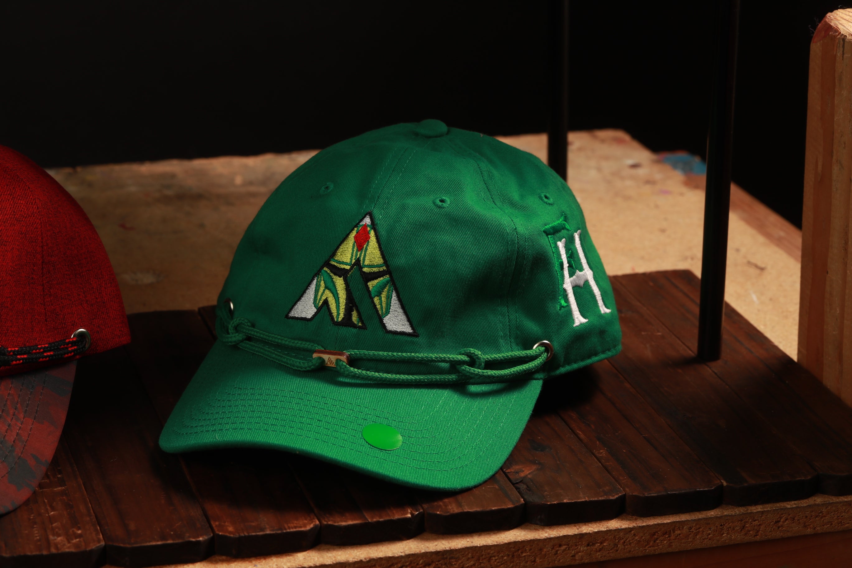 A green baseball cap with a white letter "H" on it, sitting on a wooden surface.