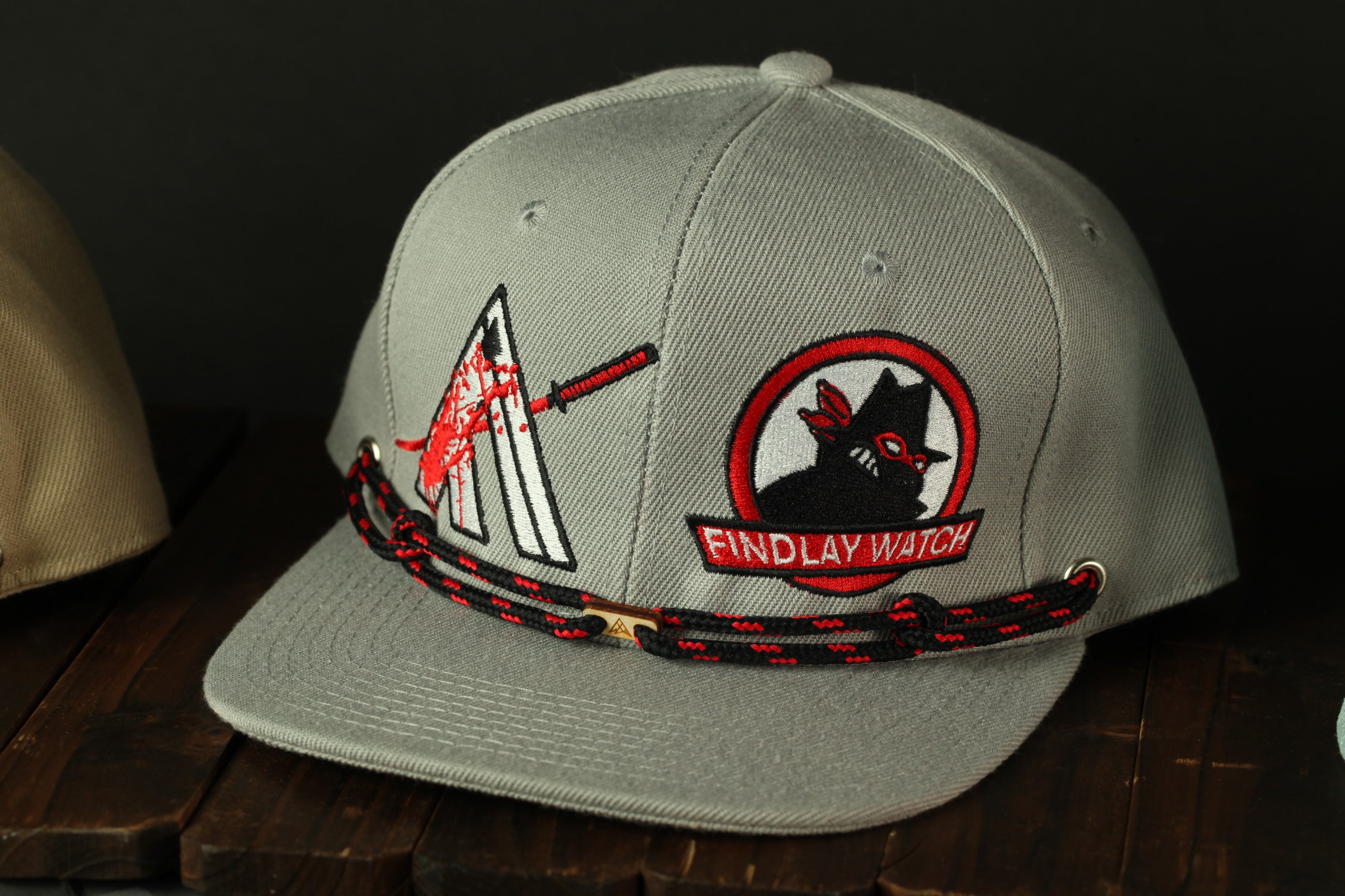 A gray baseball cap with a black and red design, including a skull and crossbones, and the text "FINDLAY WATCH" on the front.