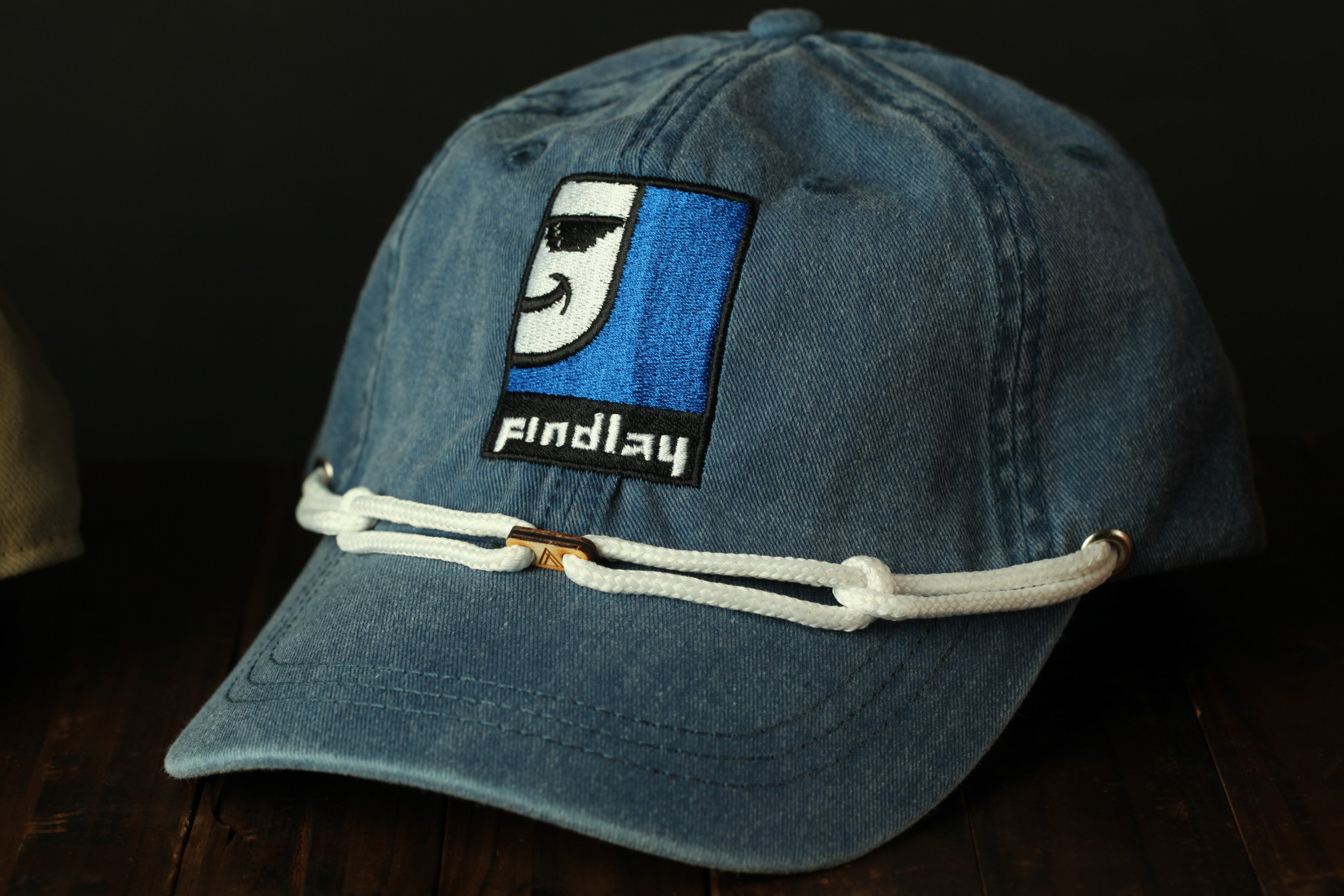 A blue denim baseball cap with a white rope strap and a patch on the front displaying a cartoon character.
