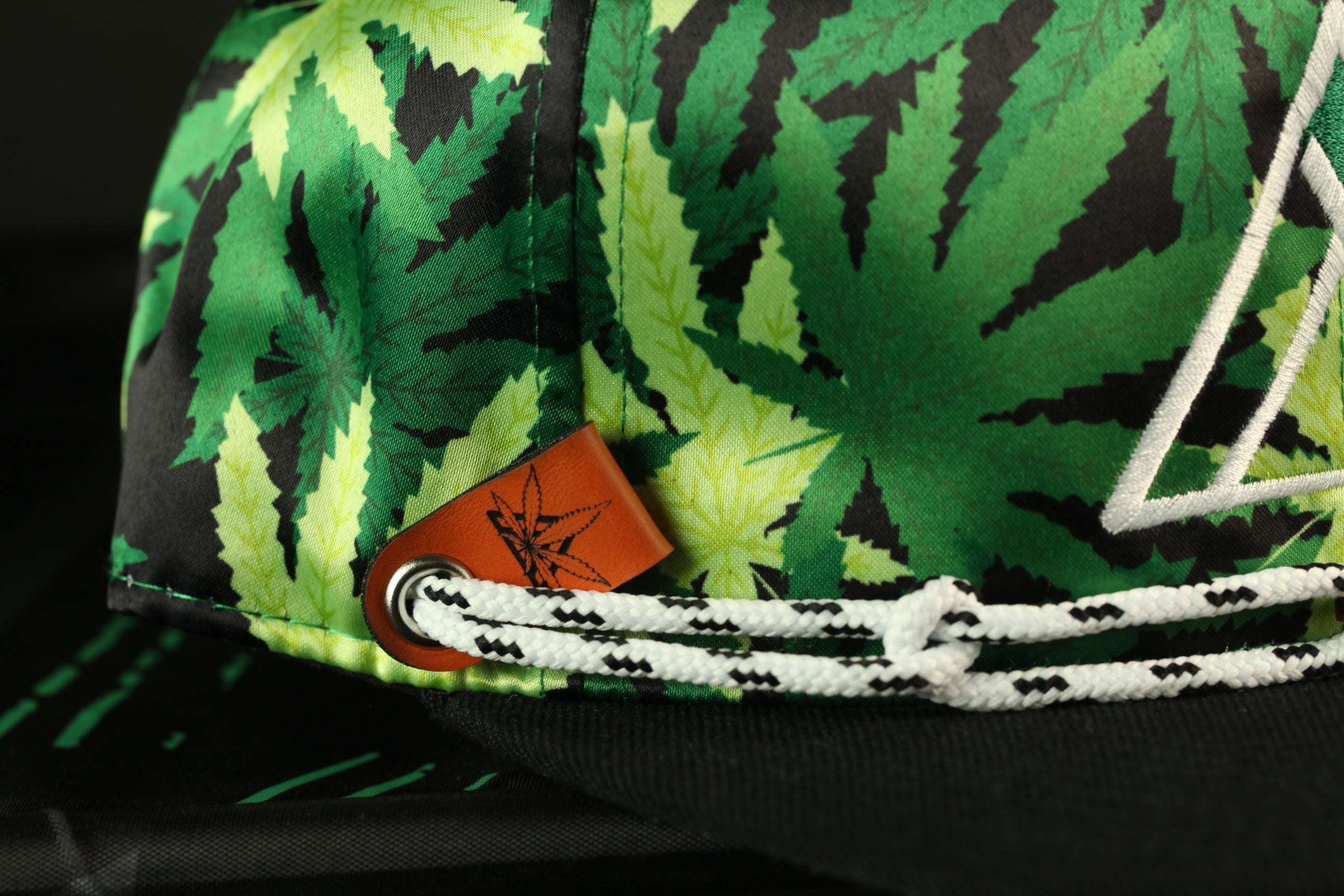 A close-up view of a colorful, leafy patterned hat with a white string and a small orange tag attached to it.