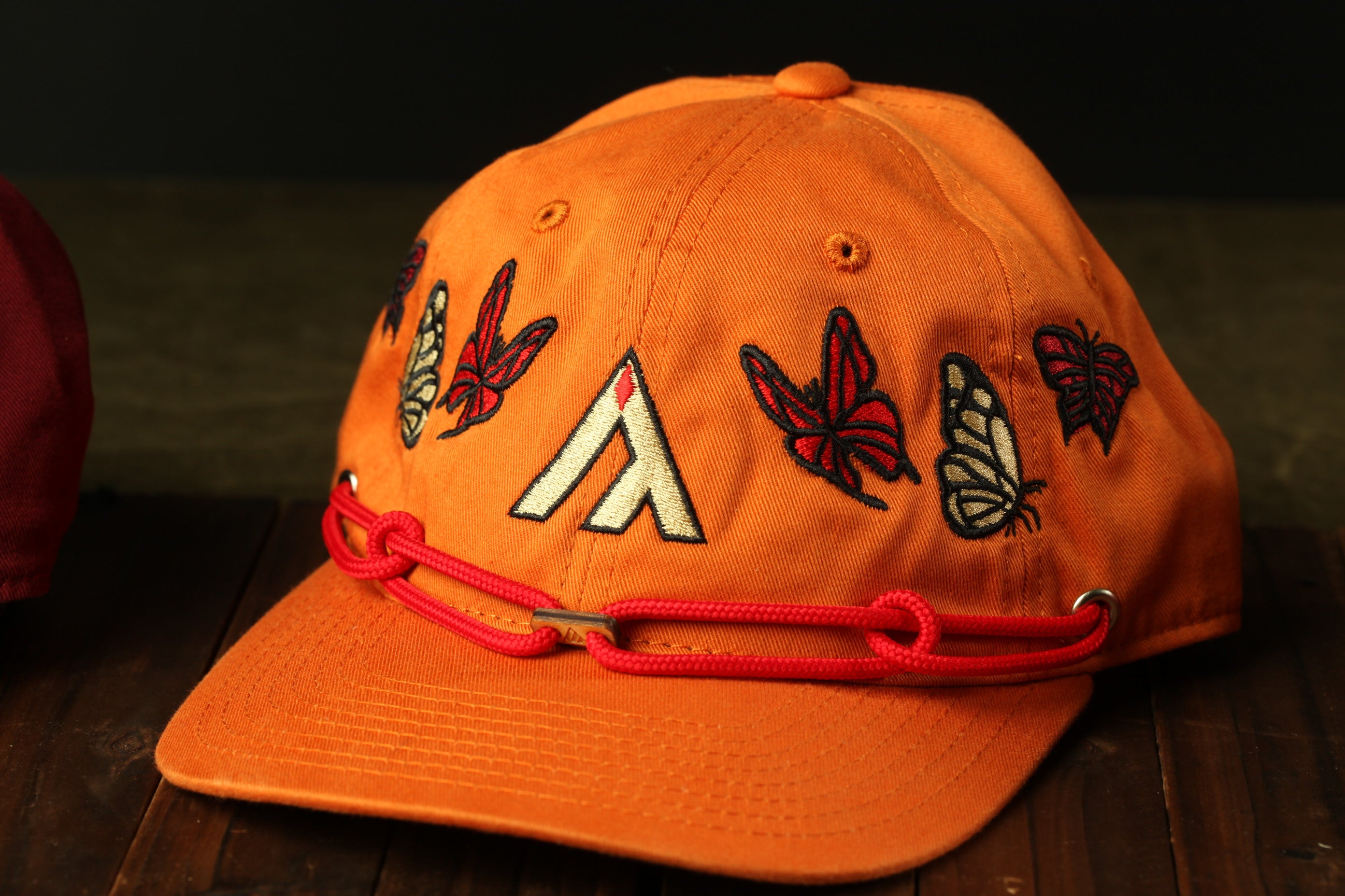 An orange baseball cap with a red string and various butterfly and symbol designs on it.
