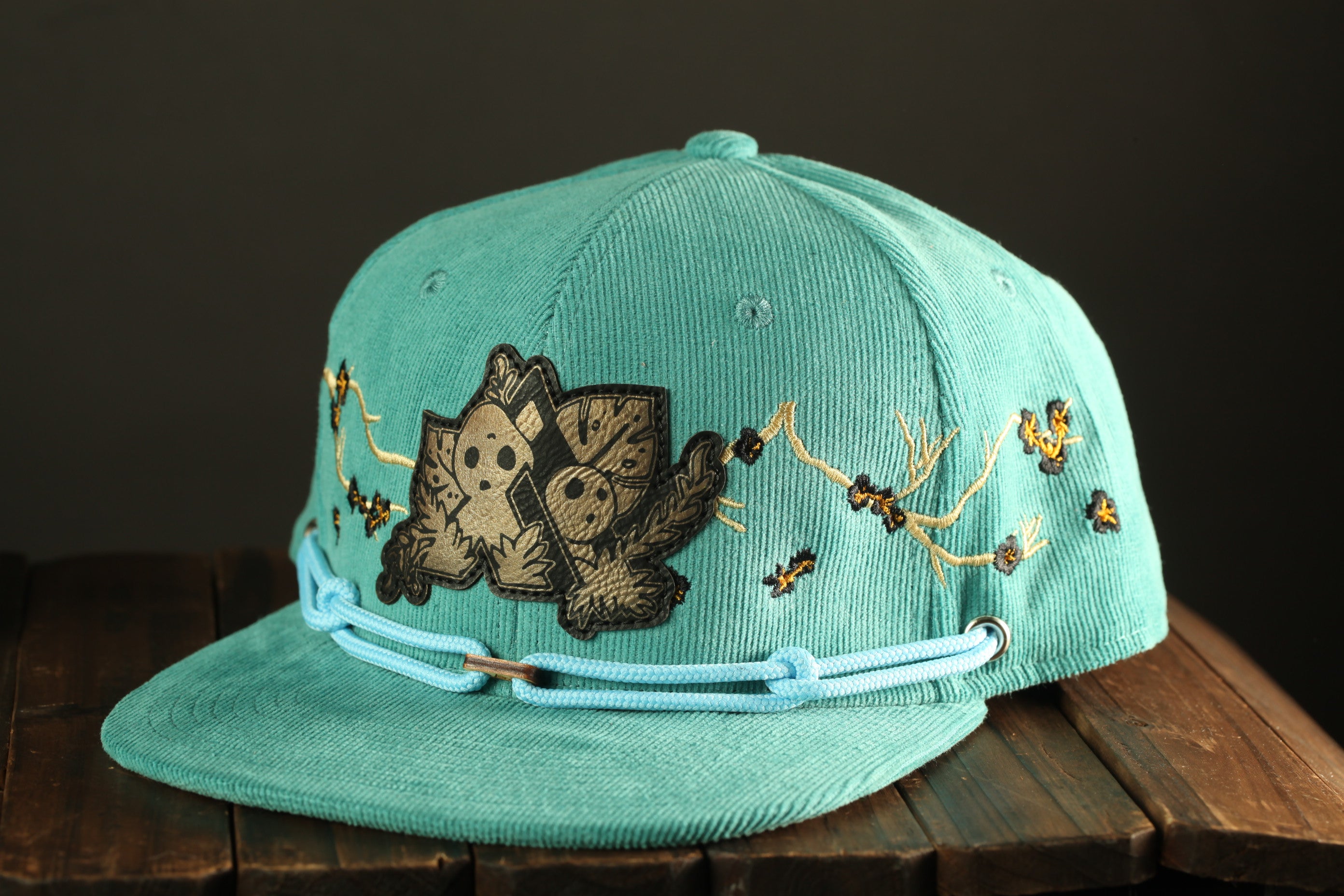 A turquoise baseball cap with a cartoon character design and floral patterns on the brim.