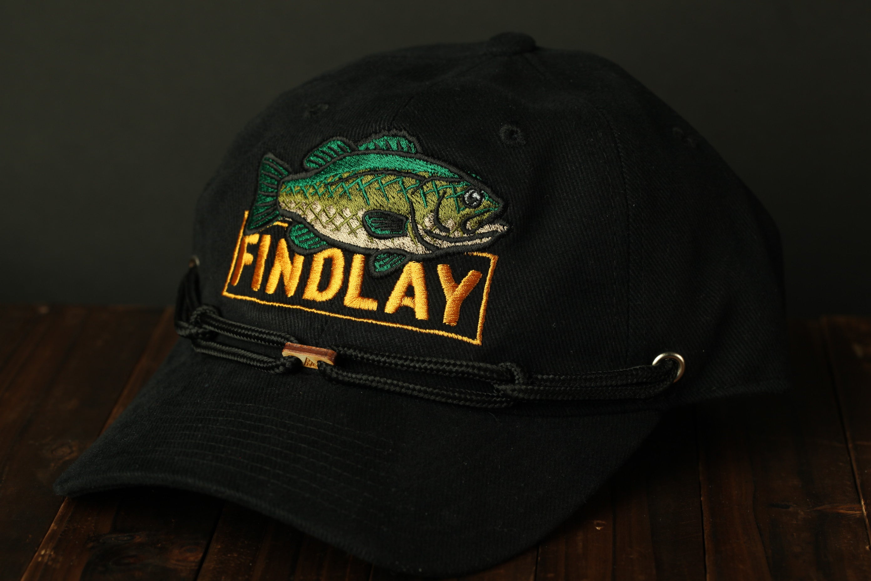 A black baseball cap with a fish embroidered on it, featuring the word "FINDLAY" in yellow text.