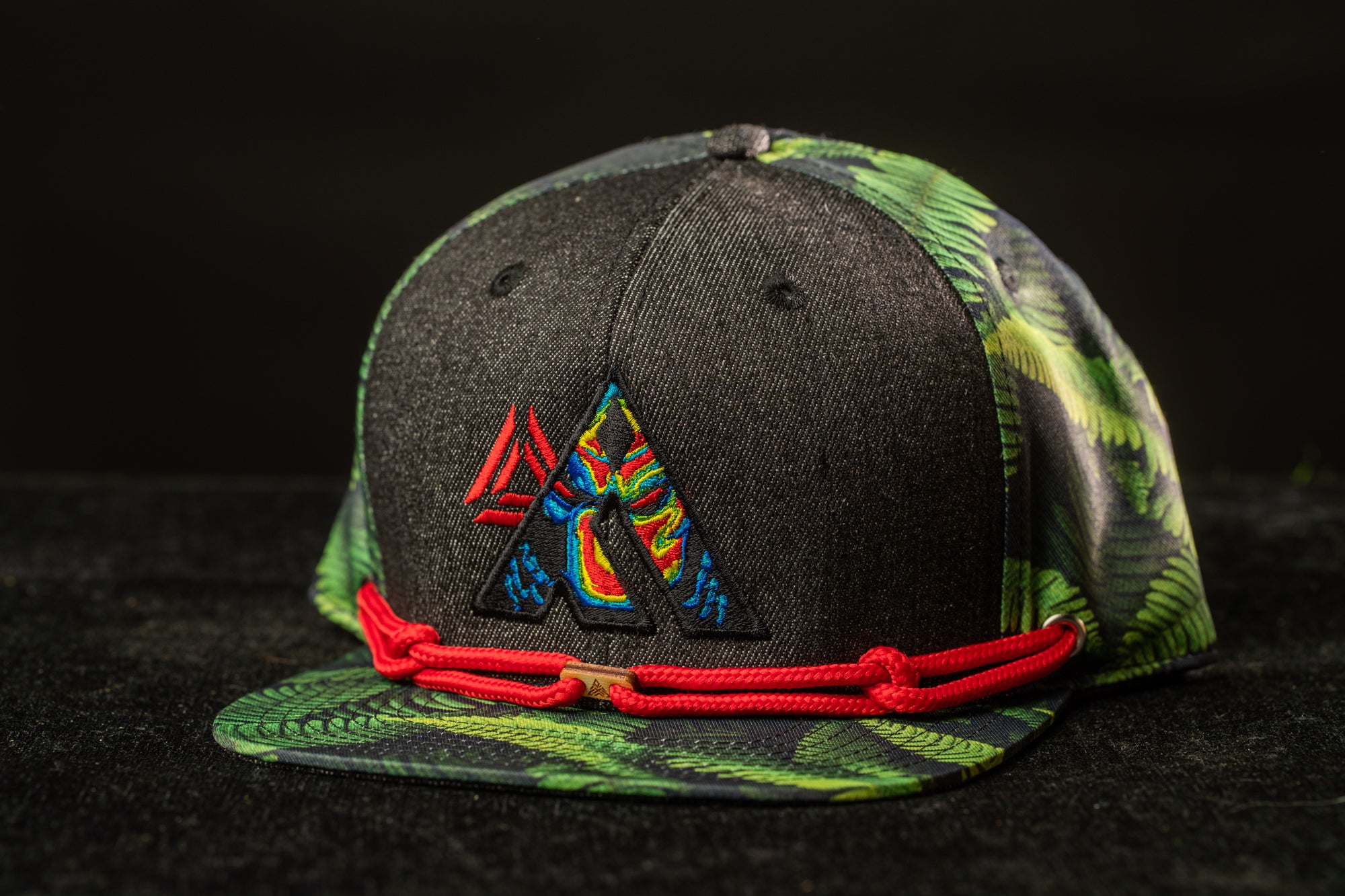 A black baseball cap with a colorful, patterned design and a red string around the brim.