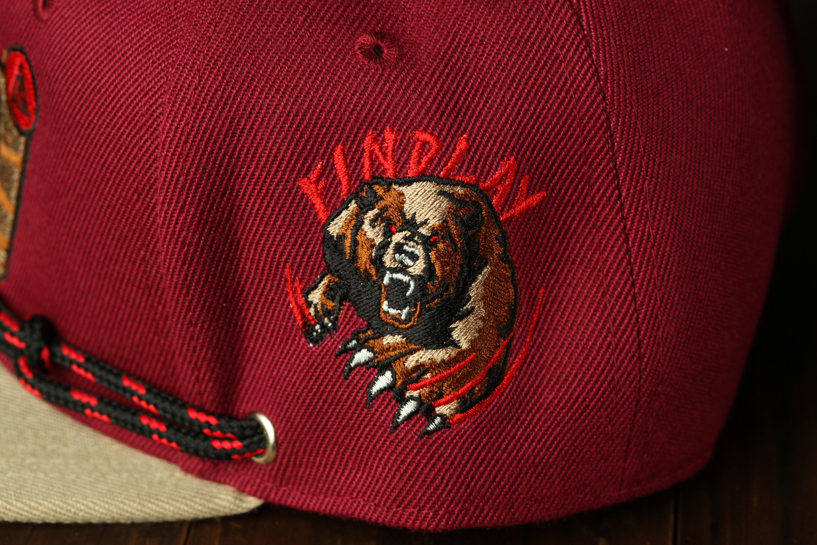 A close-up view of a maroon baseball cap with a large embroidered bear on the front.