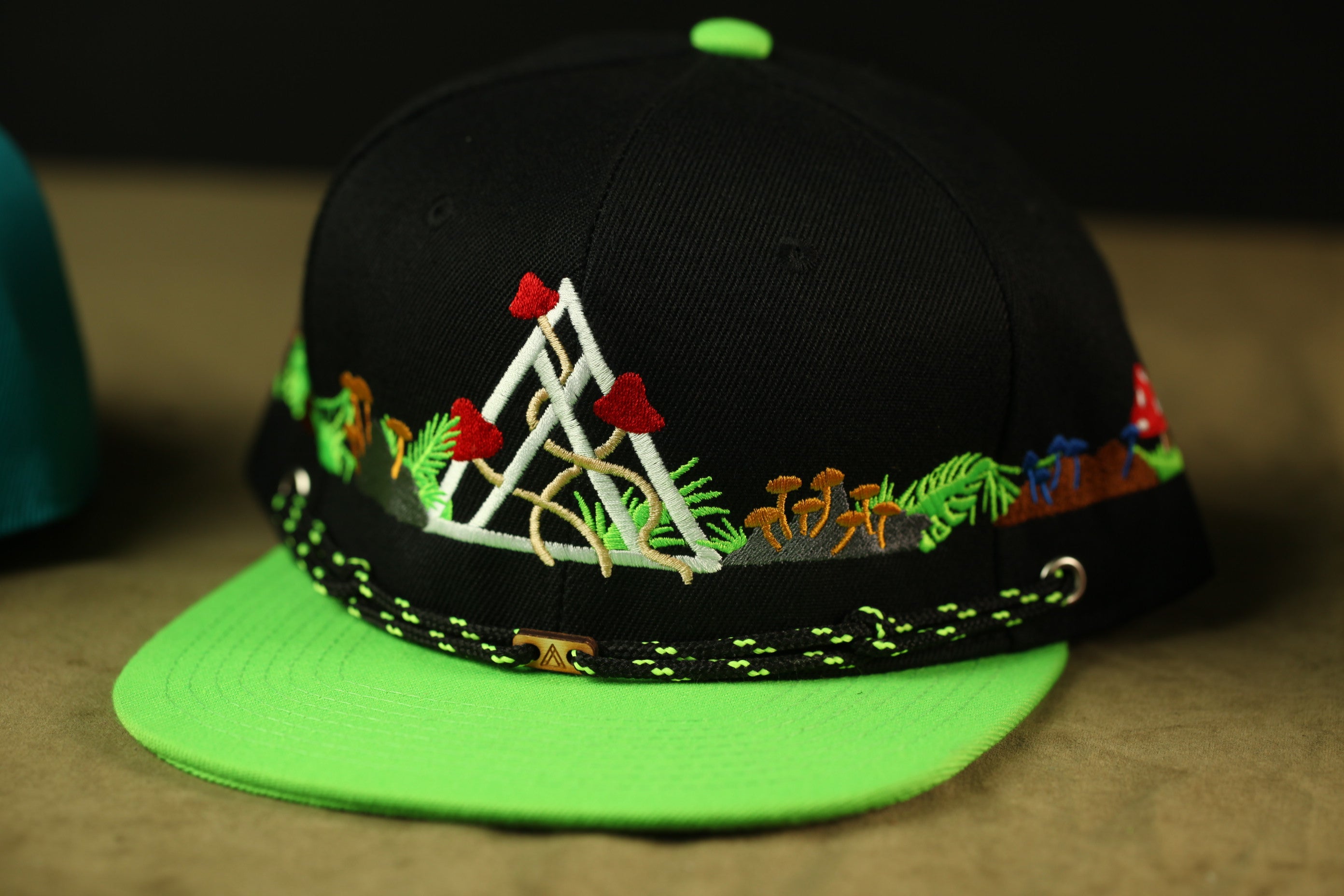 A black baseball cap with a green brim and colorful floral embroidery on the front.