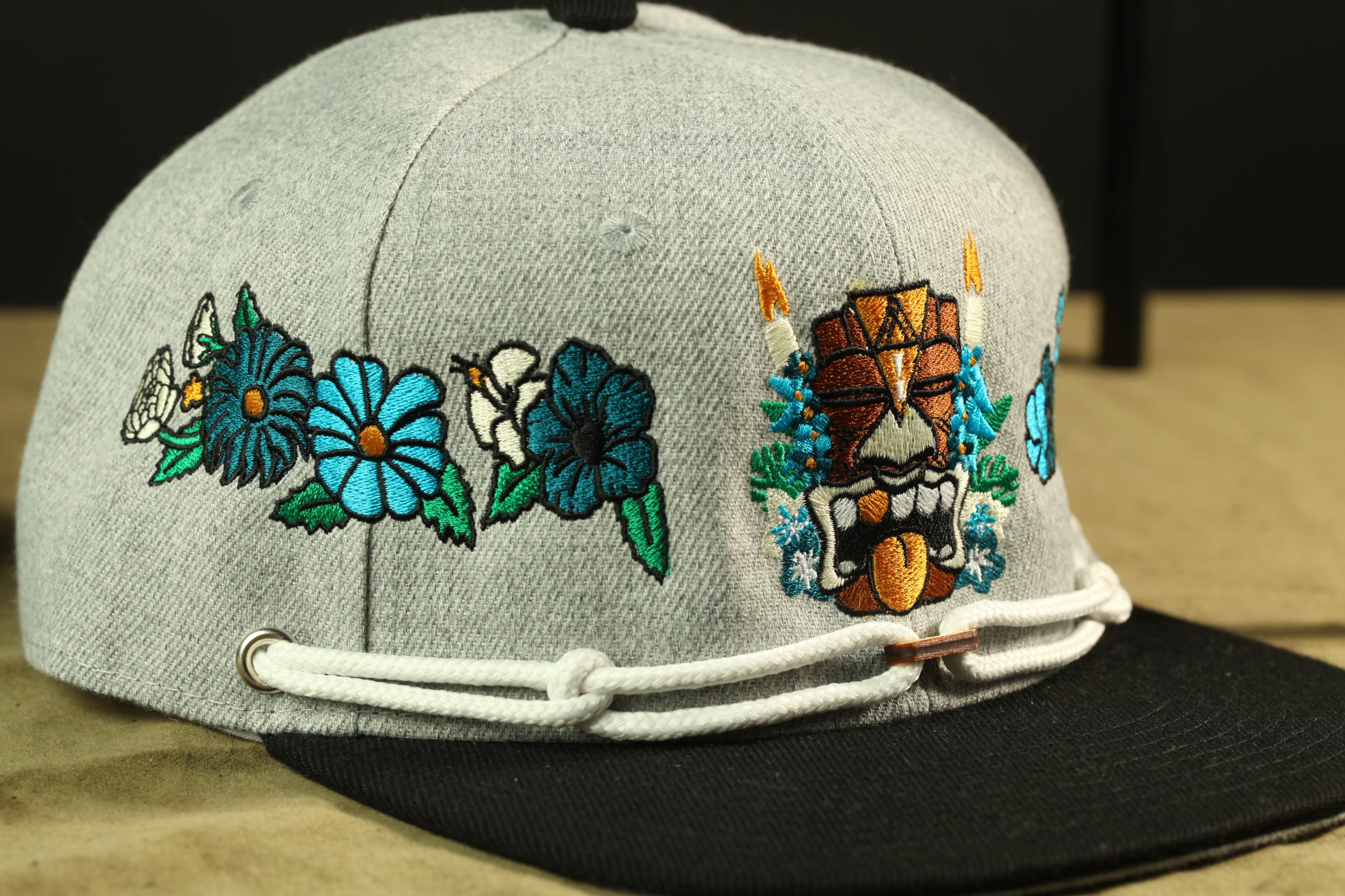 A gray baseball cap with colorful floral and tiki-style embroidered designs on the front.