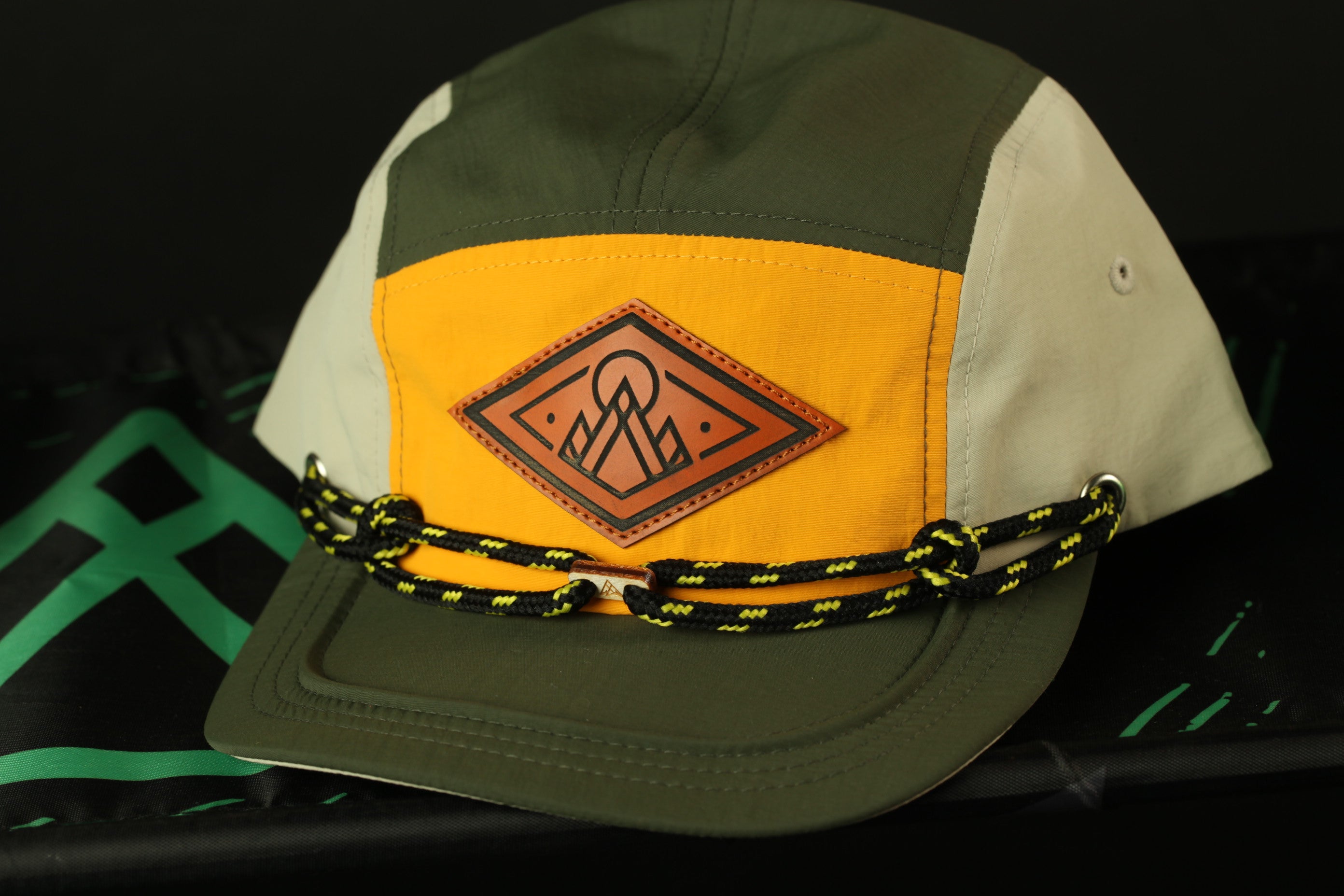 A green and yellow baseball cap with a leather patch and black and yellow rope strap.