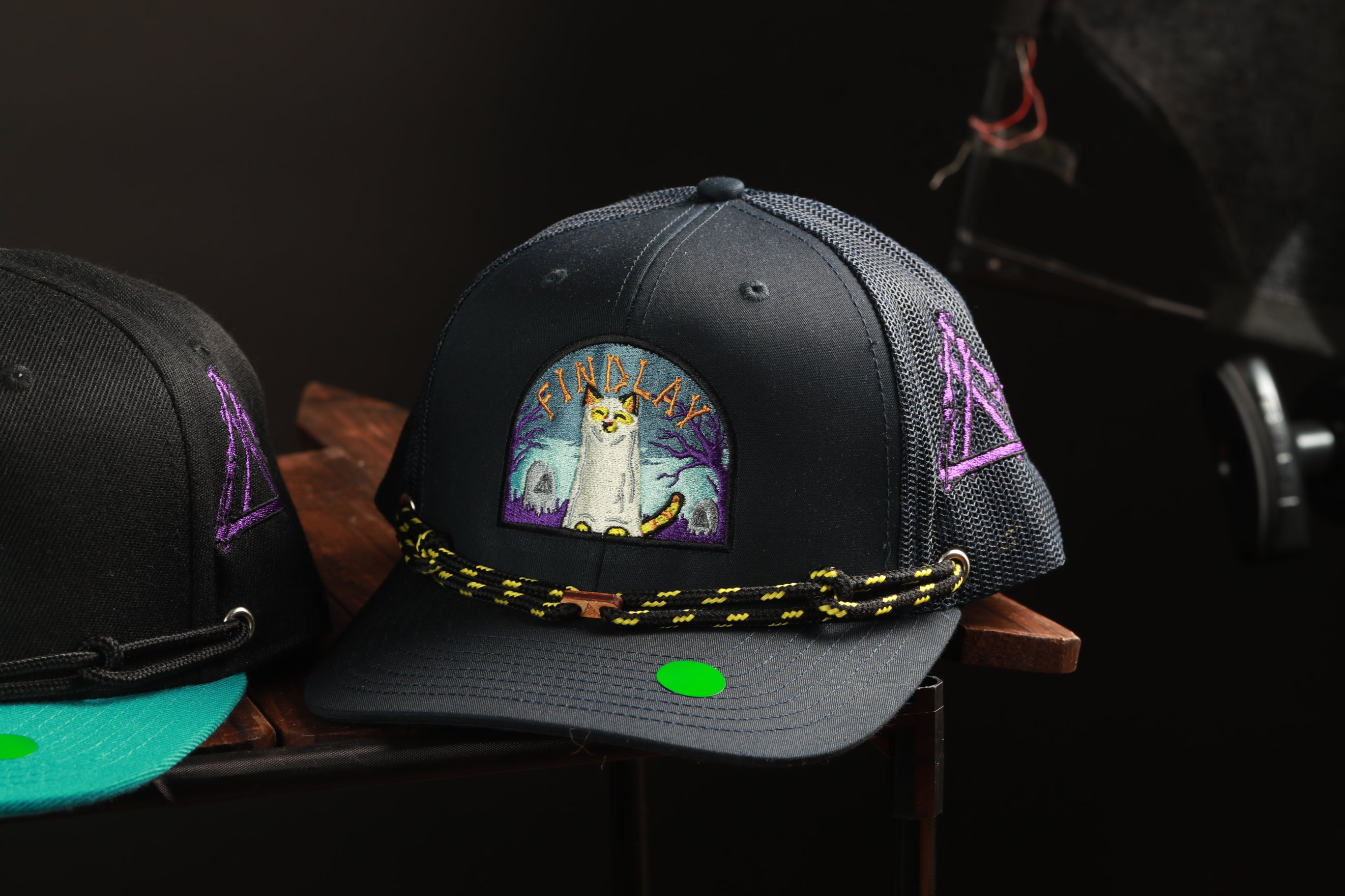 A black baseball cap with a colorful graphic and a purple and yellow design on the front, displayed on a wooden surface.