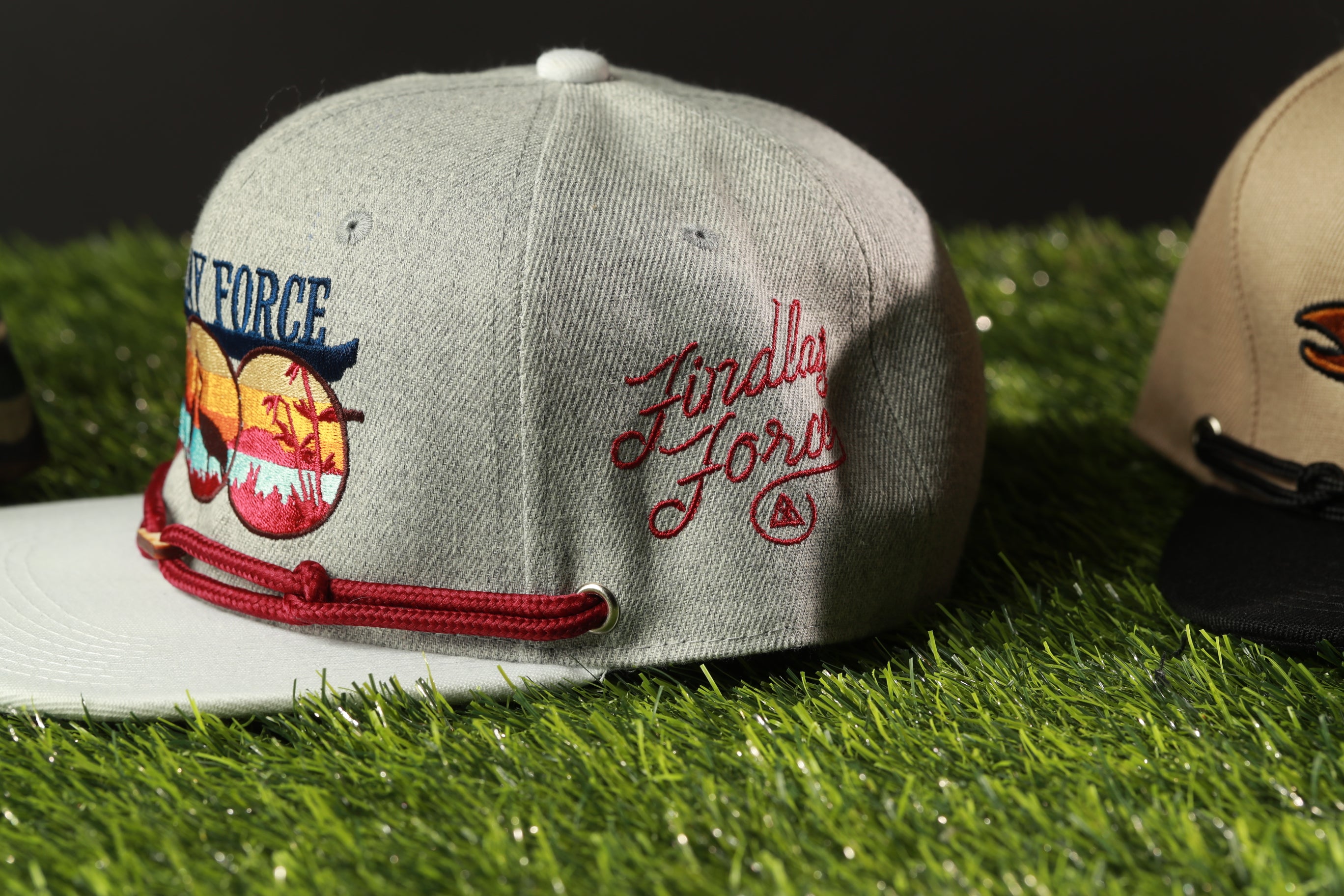 A gray baseball cap with red and blue embroidered designs, placed on a grassy surface.