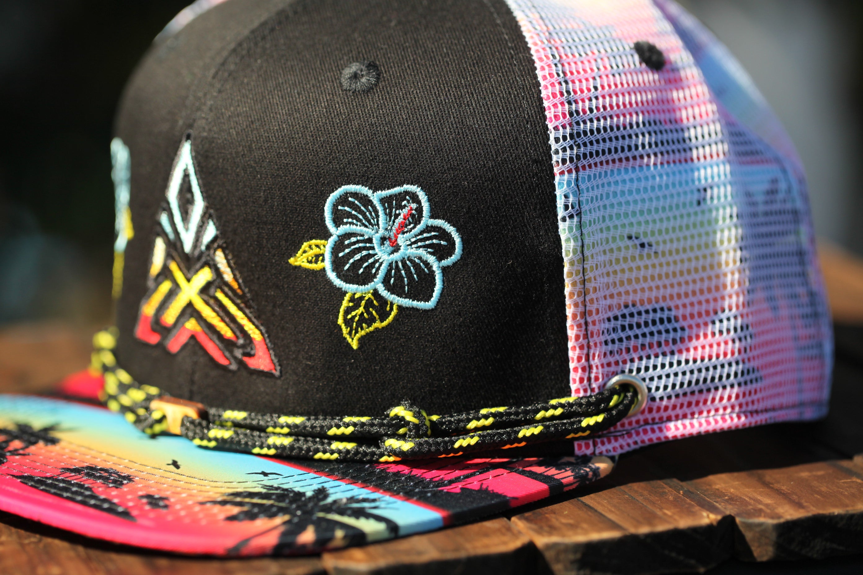 A colorful baseball cap with a floral embroidered design and a patterned brim, resting on a wooden surface.