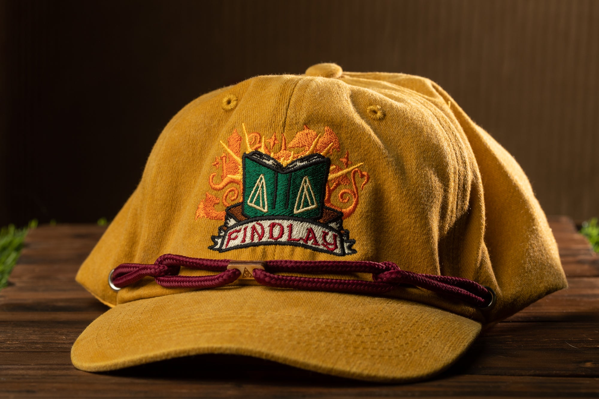 A yellow baseball cap with a green and orange design on the front, featuring the text "FINDLAY" and a graphic of a book.