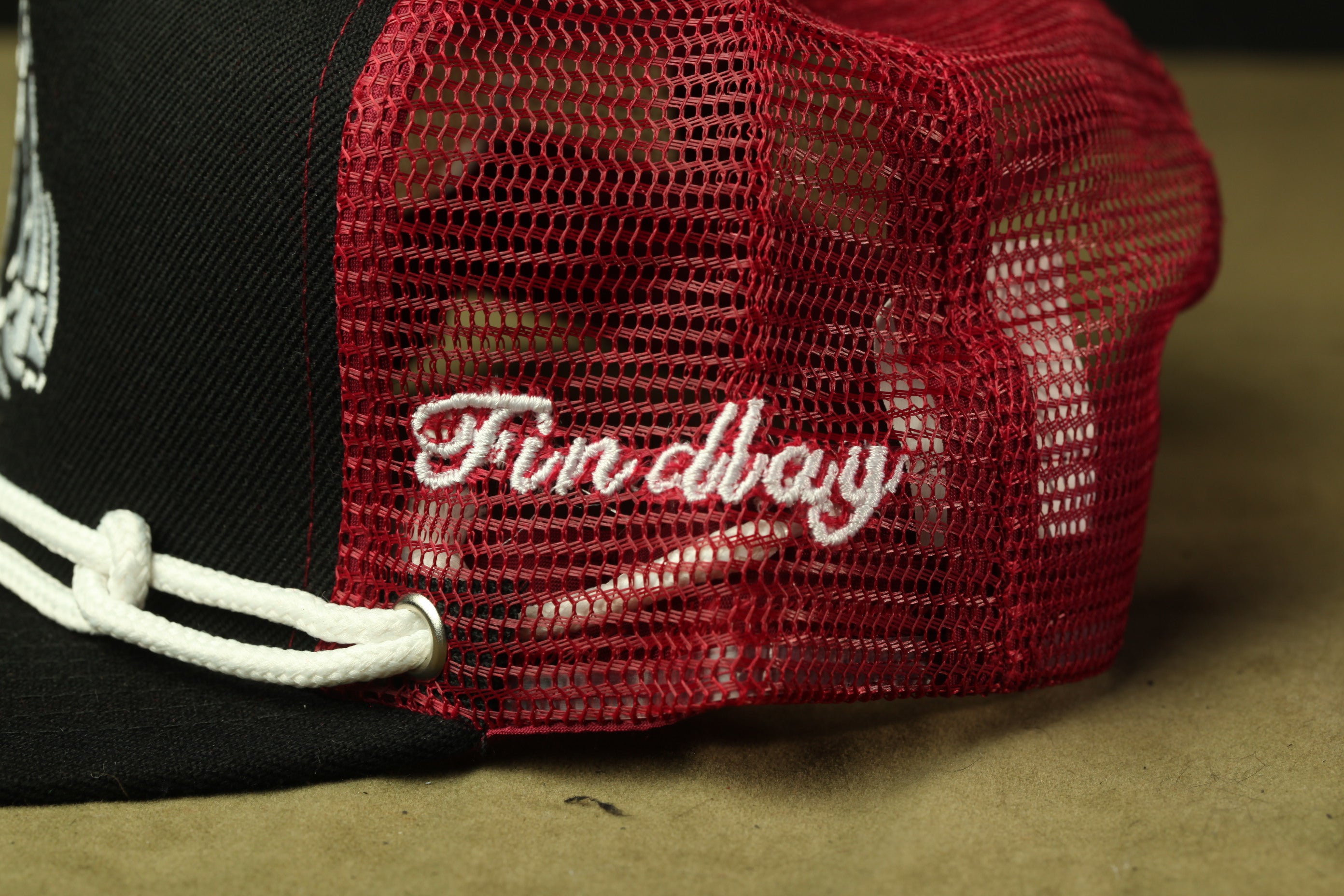 A close-up view of a red mesh fabric on a black fabric, with the word "Funday" embroidered on it.