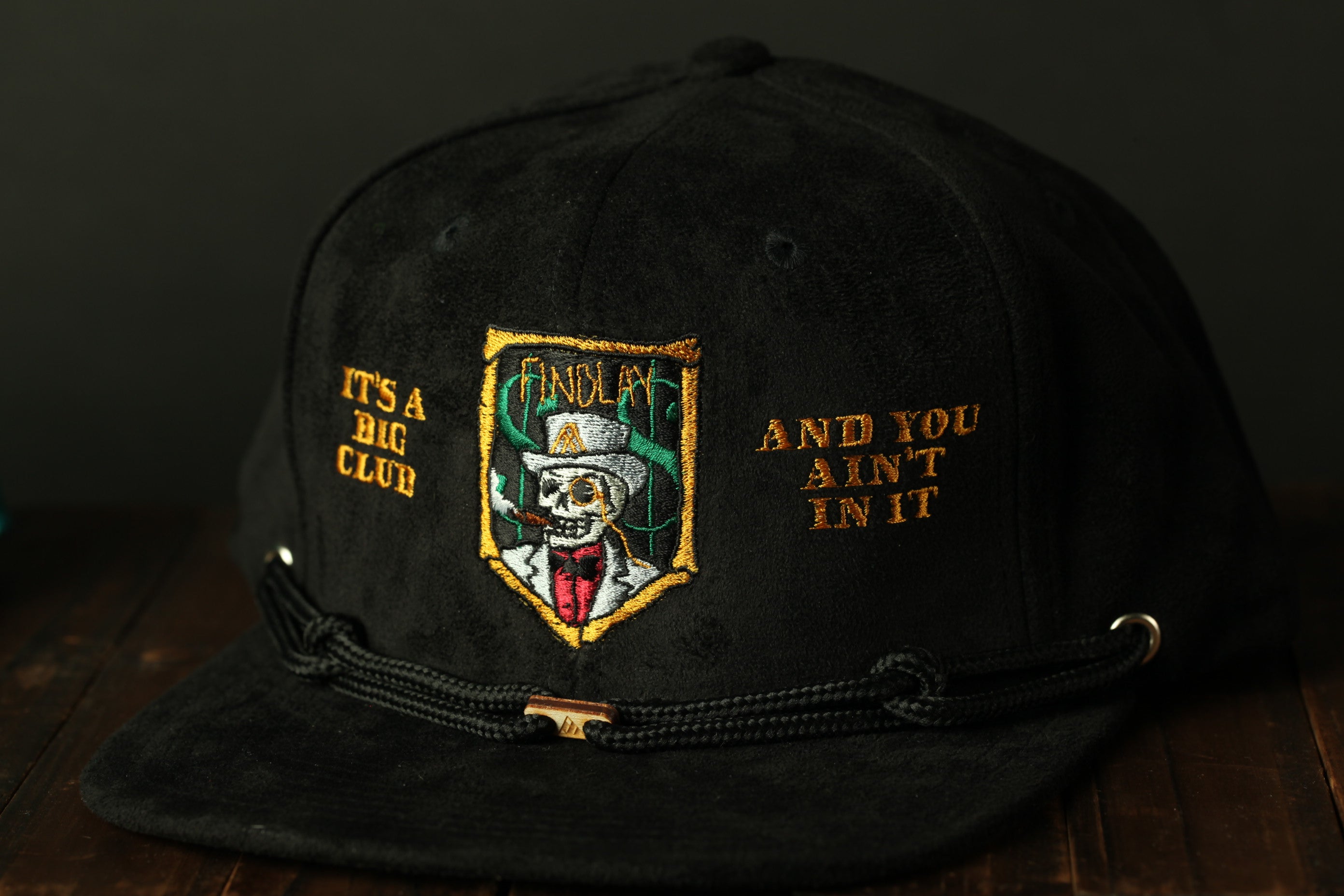 A black baseball cap with a gold and red embroidered design on the front, featuring a skull and crossbones symbol.