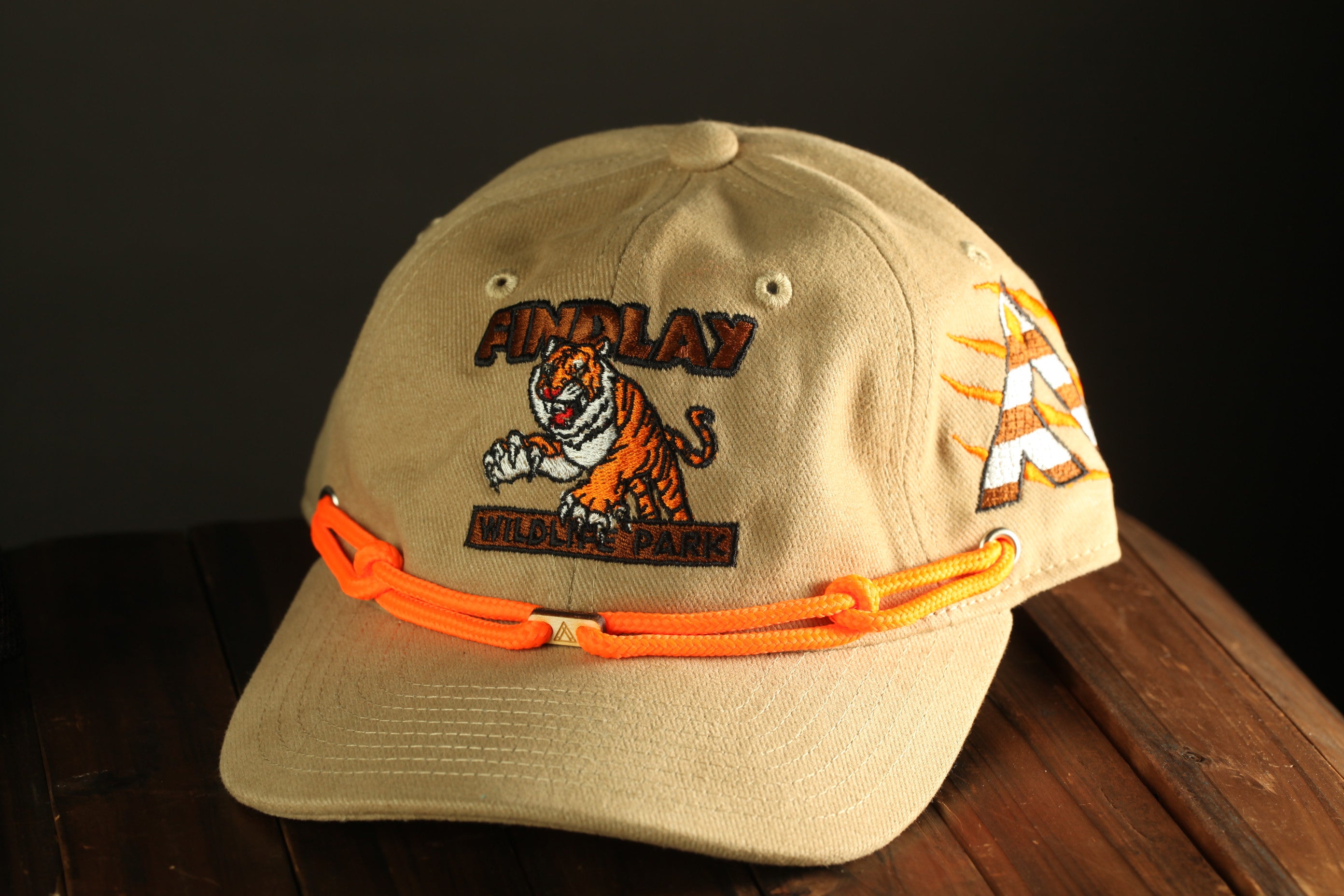 A tan baseball cap with an orange and white tiger design and the text "FINDlay Wildlife Park" printed on it.
