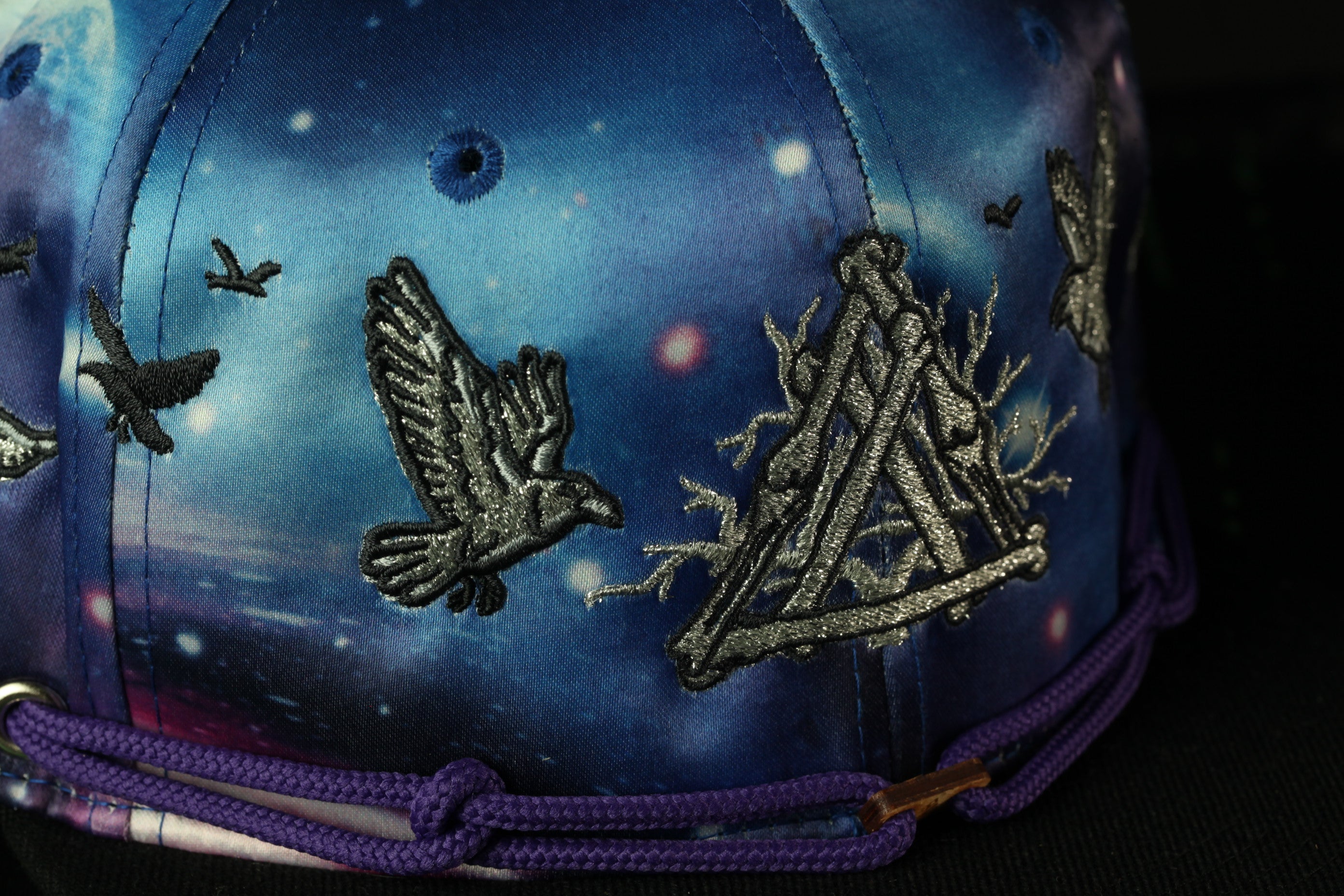 a close-up view of a colorful, patterned baseball cap with various designs and details, including a bird motif and a triangular pattern.