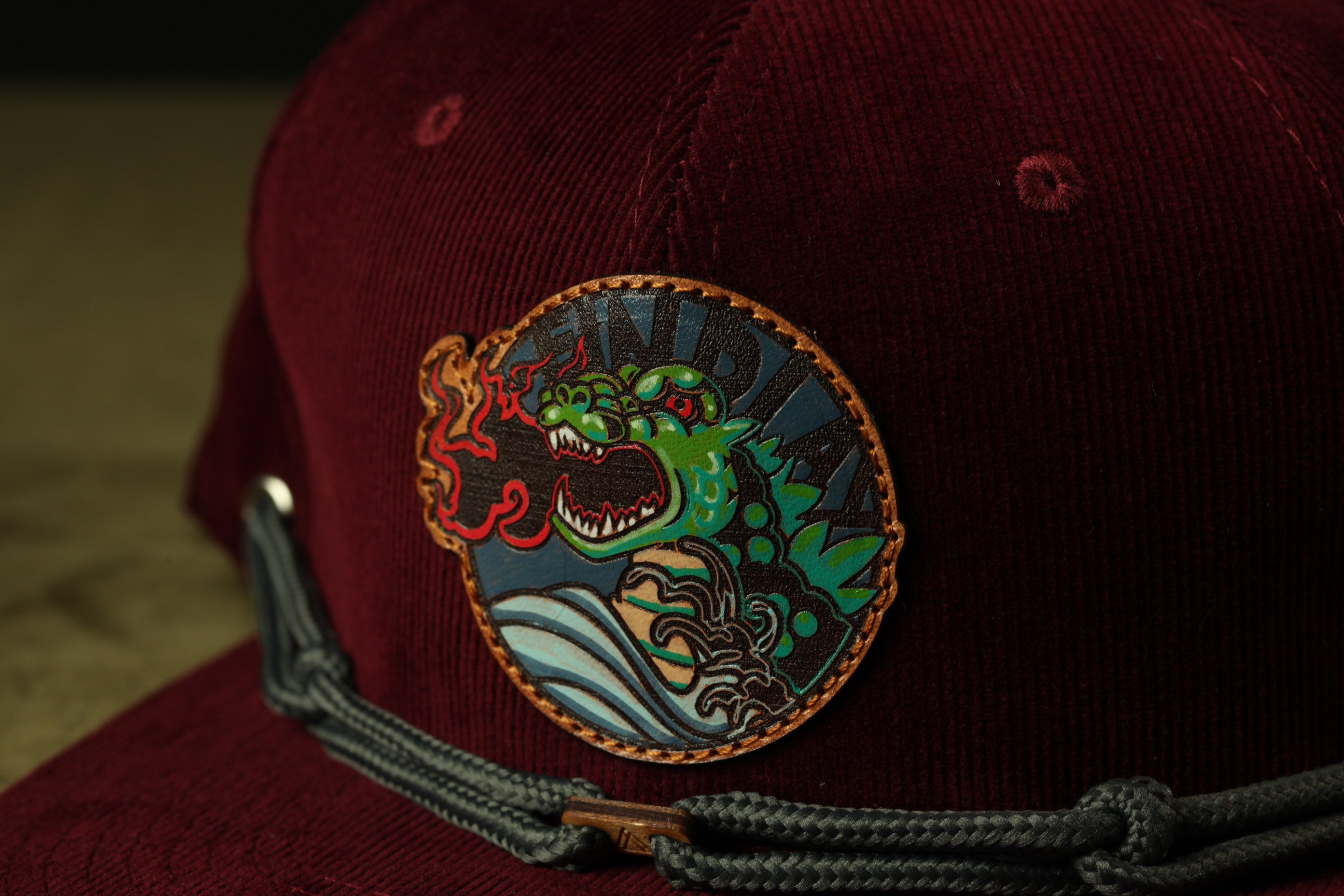 A close-up view of a burgundy baseball cap with a circular patch featuring a green dragon and the word "INDIA" printed on it.