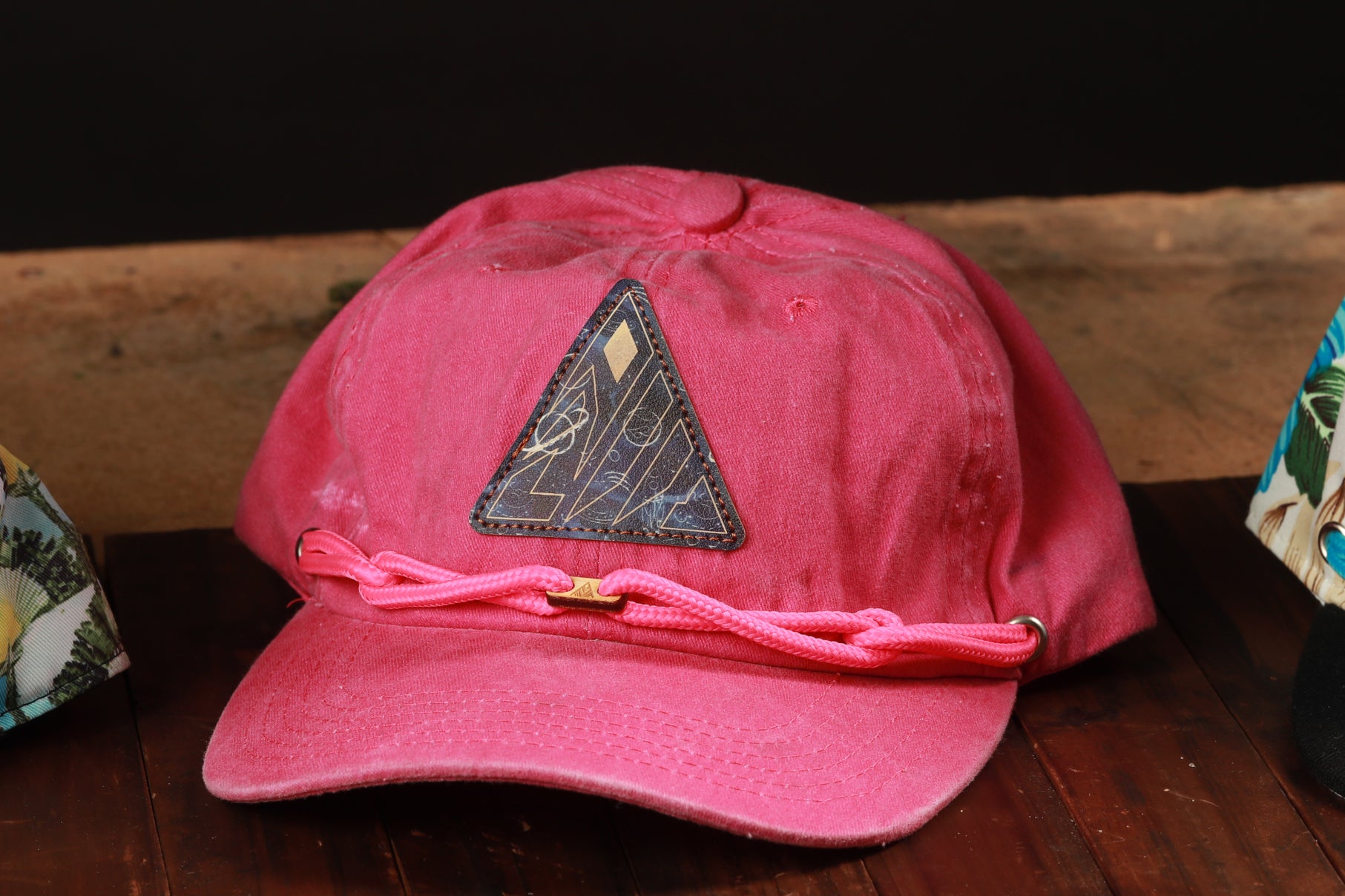 A pink baseball cap with a triangular patch on the front, sitting on a wooden surface.
