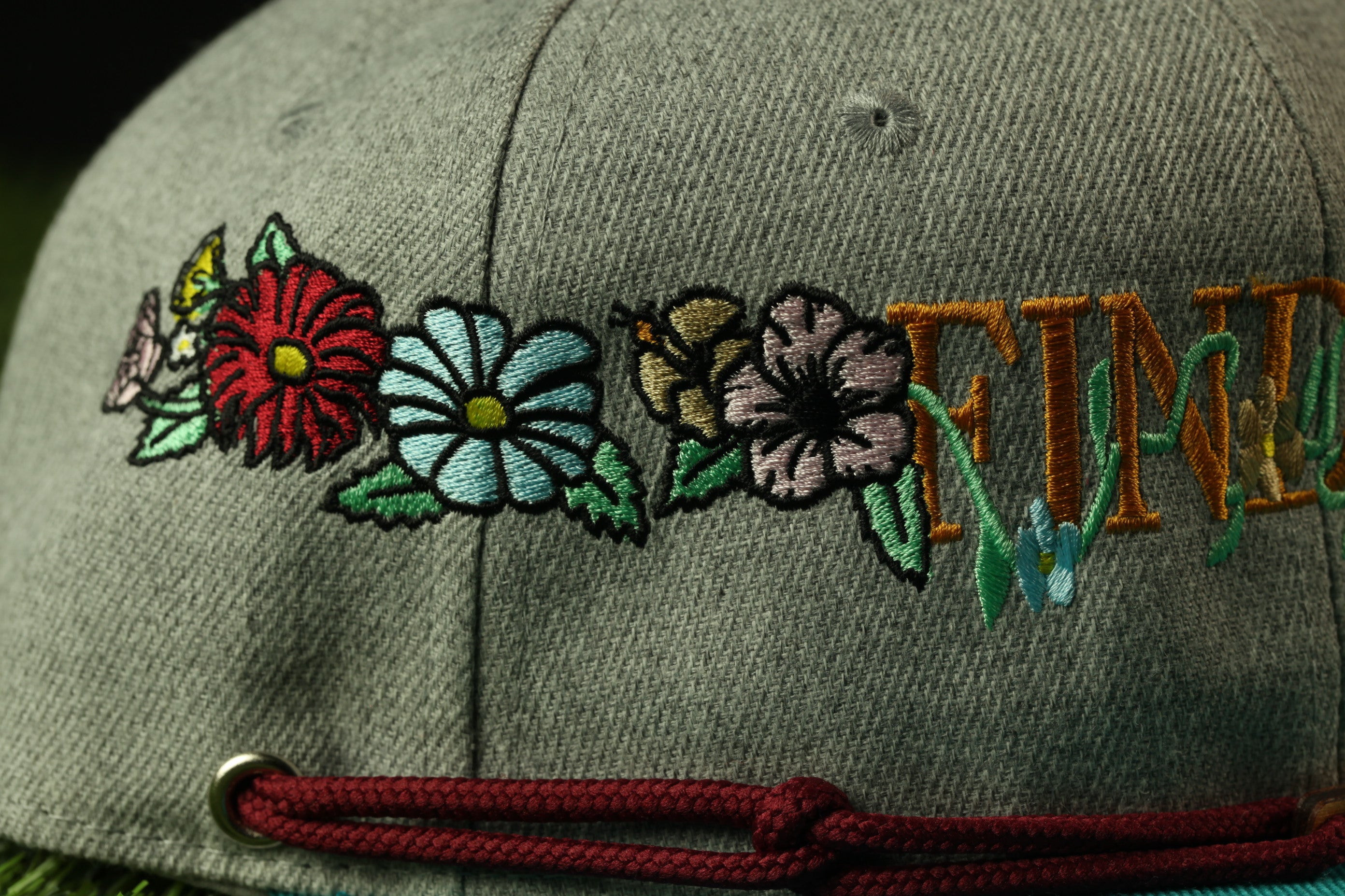 A close-up view of a gray baseball cap with colorful floral embroidery and the word "FEMININE" embroidered on it.