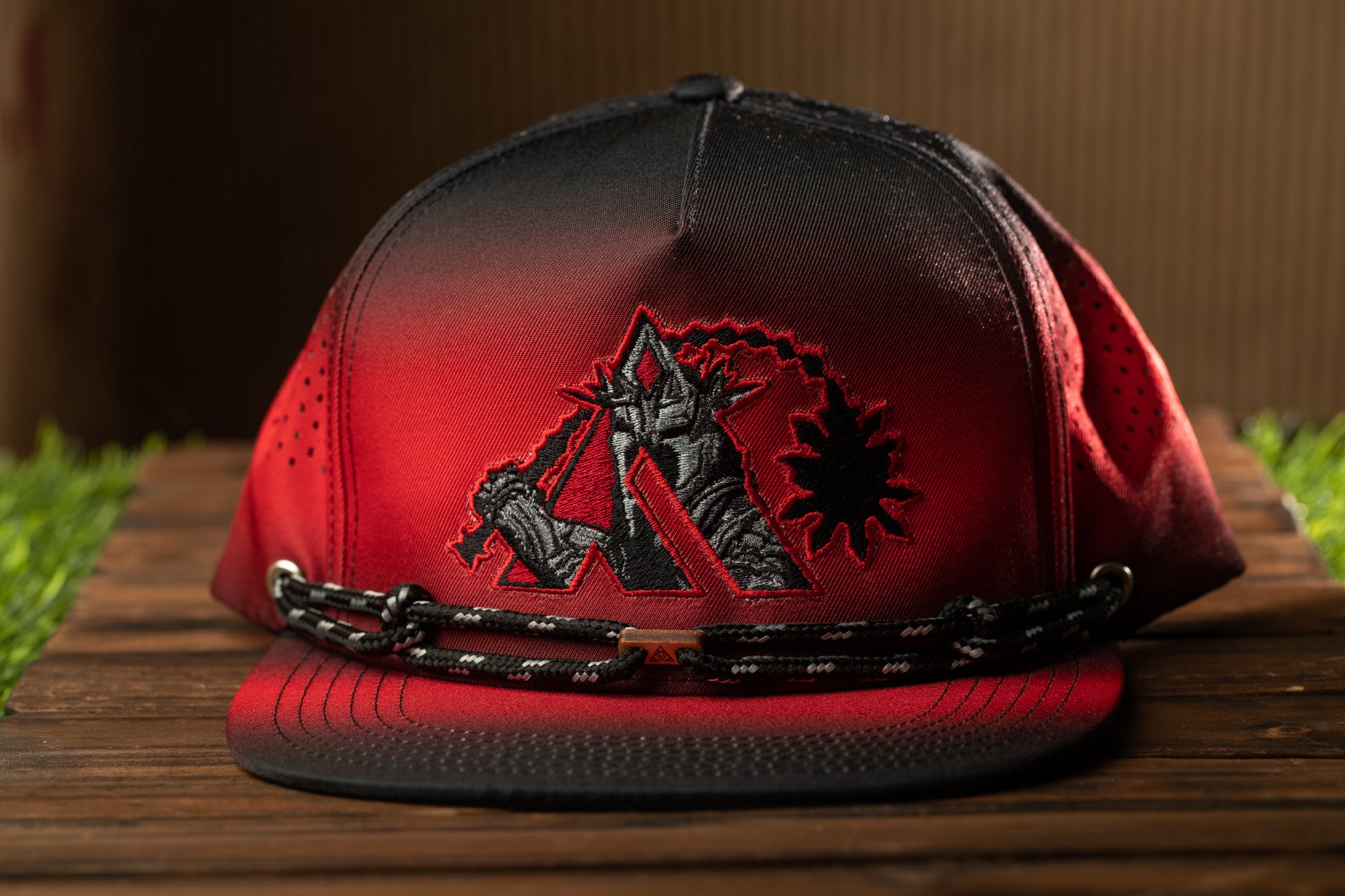 A red baseball cap with a black and red design on the front, featuring a stylized figure and a sun-like symbol.