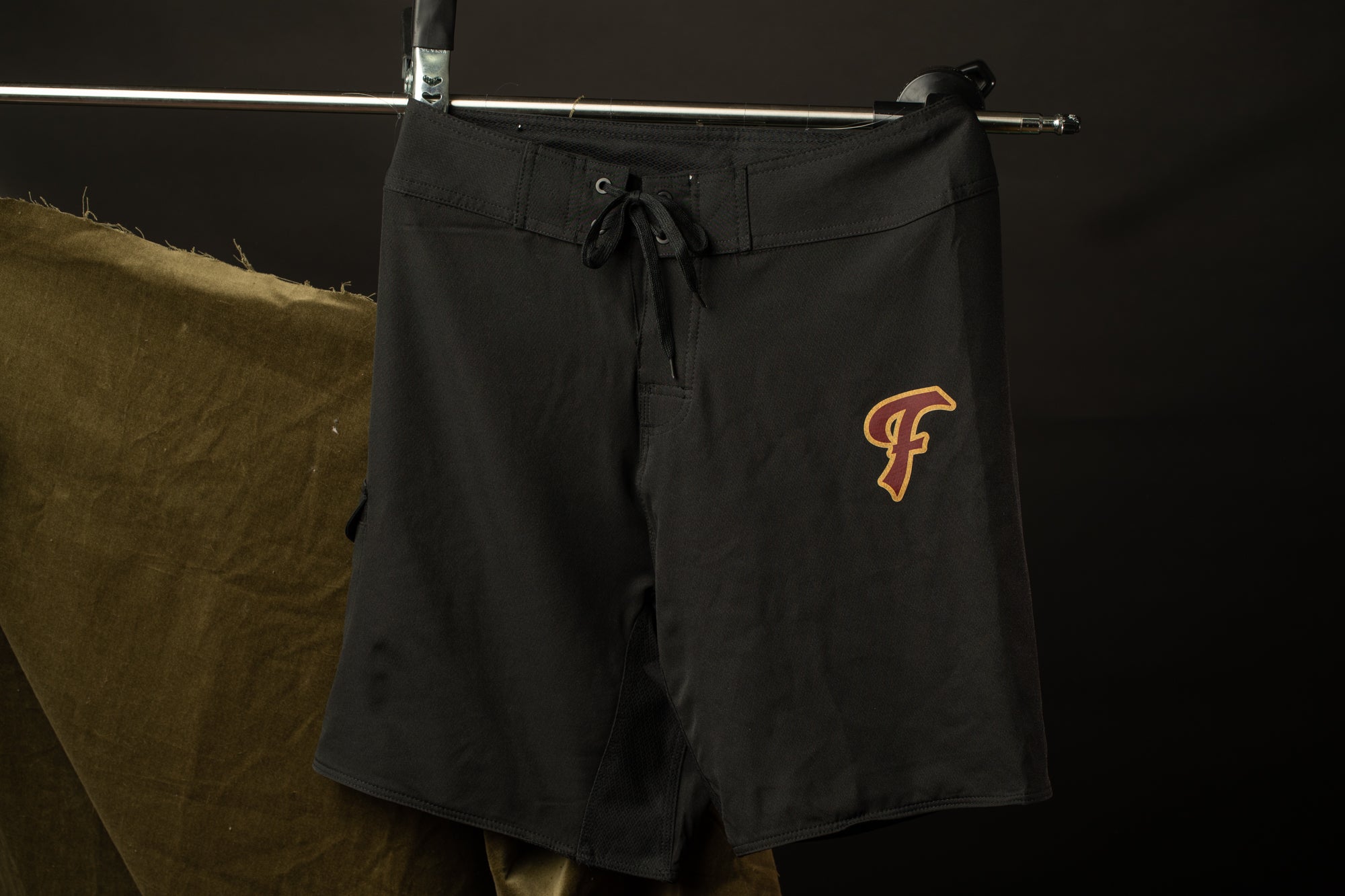 A pair of black shorts with a large "F" logo on the side, hanging on a clothing rack against a dark background.