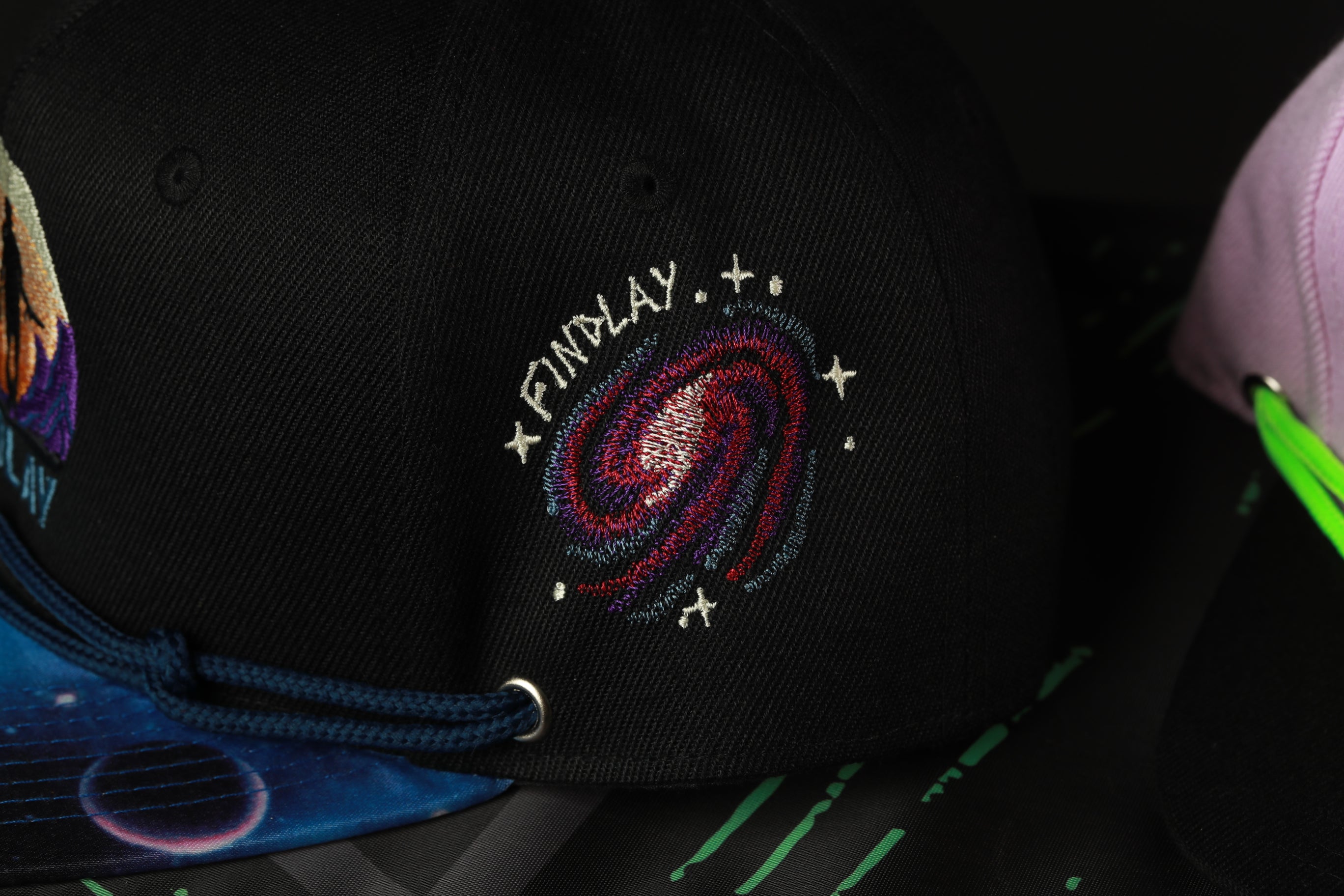 a close-up view of a black baseball cap with a colorful galaxy embroidered on it.