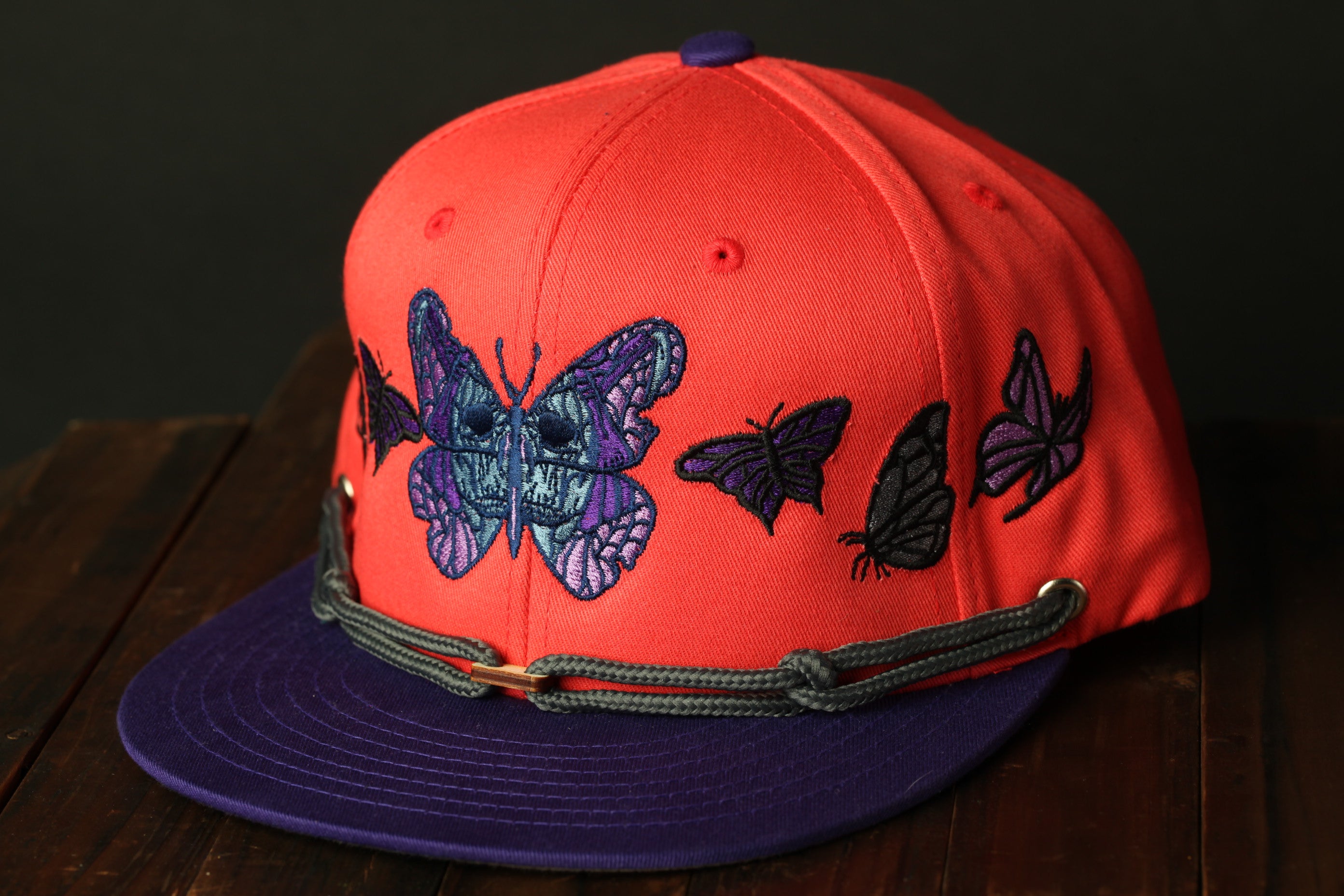 A red baseball cap with a purple and blue butterfly design on the front.