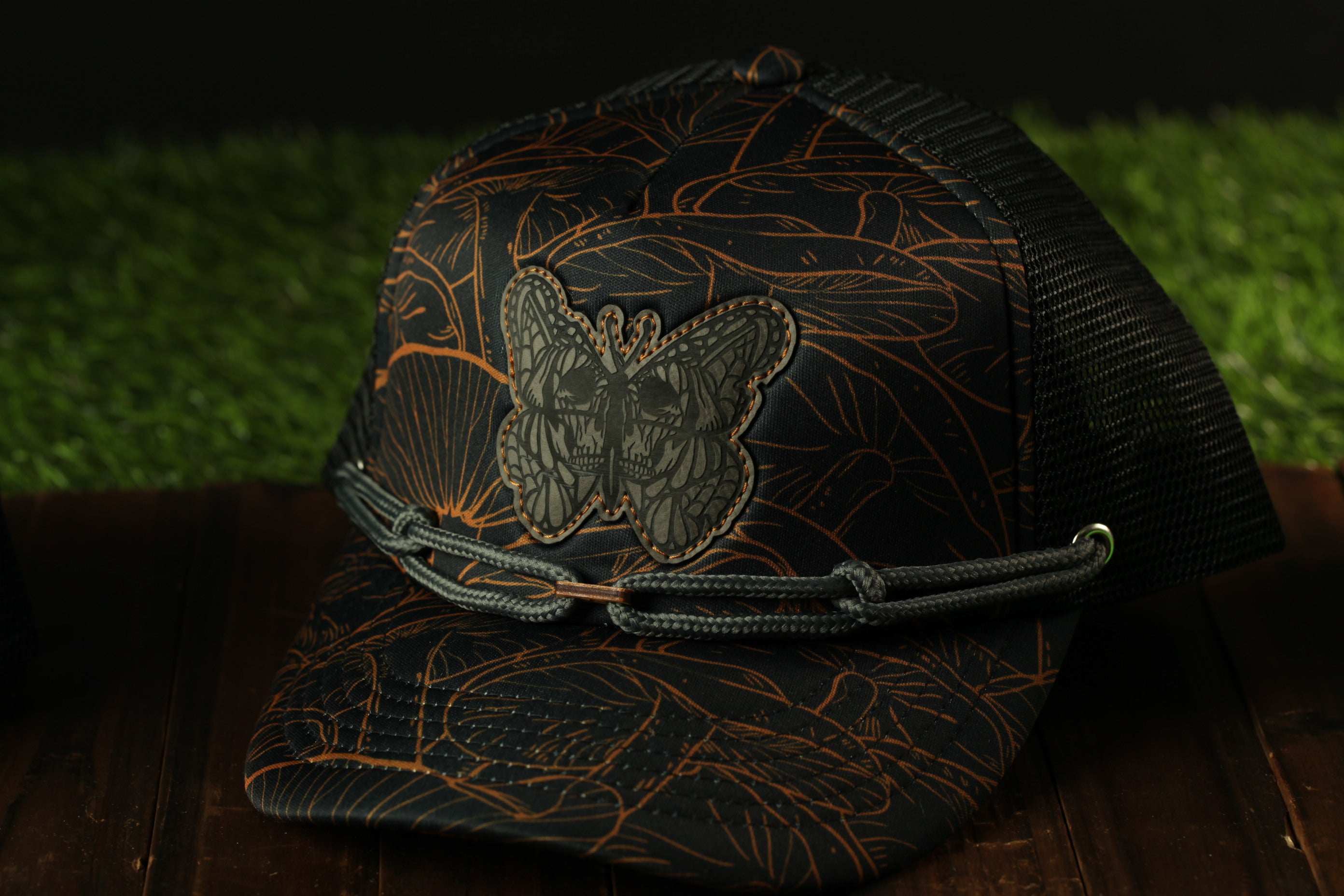 A black baseball cap with a butterfly design on the front, sitting on a wooden surface.