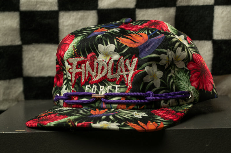 A colorful floral cap with the text "FIND LAY" printed on it, sitting on a surface against a checkered background.