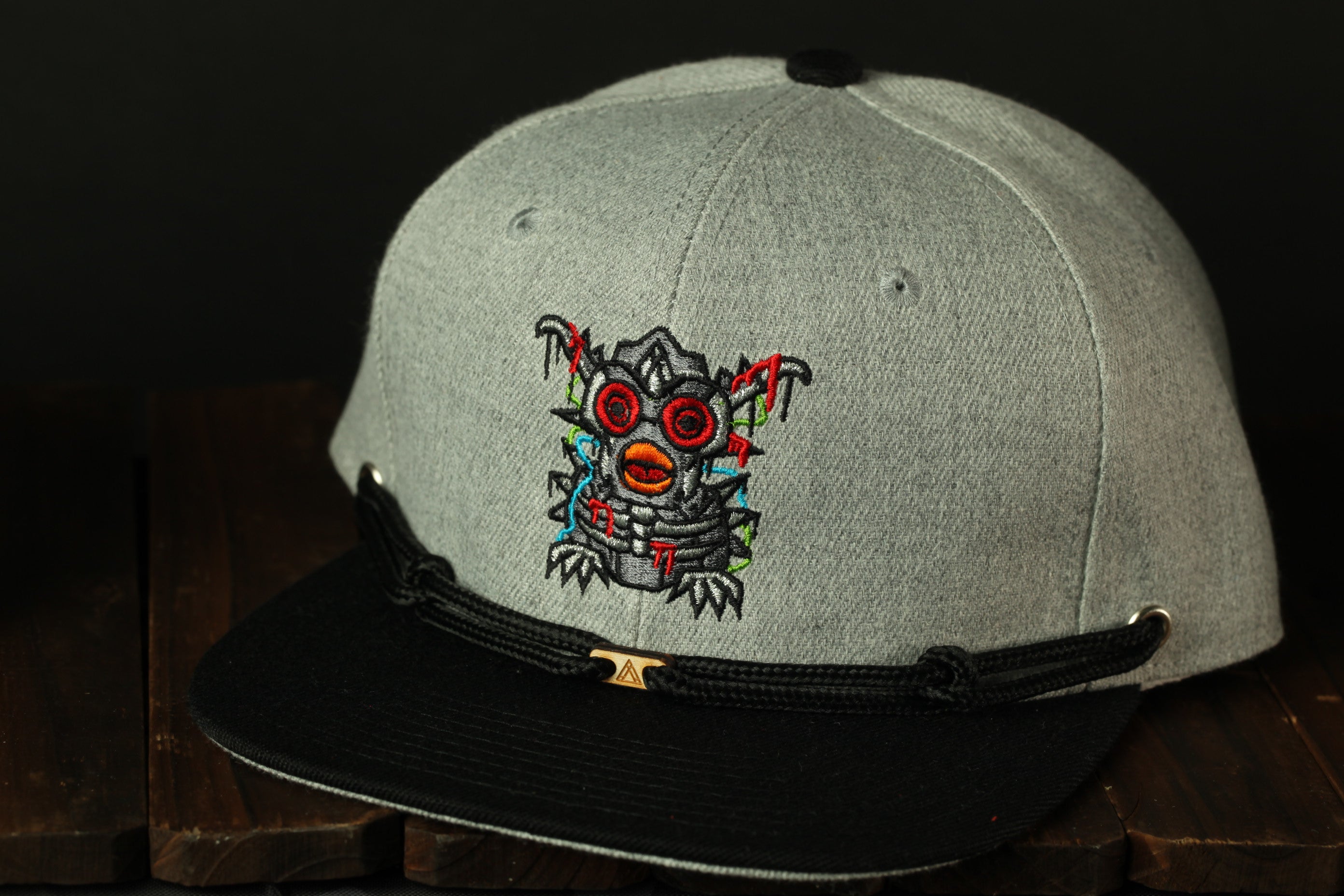A gray baseball cap with a black brim and a unique embroidered design on the front.