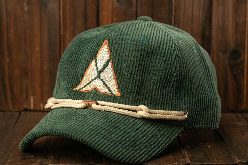 A green baseball cap with a white and orange embroidered logo on the front, resting on a wooden surface.