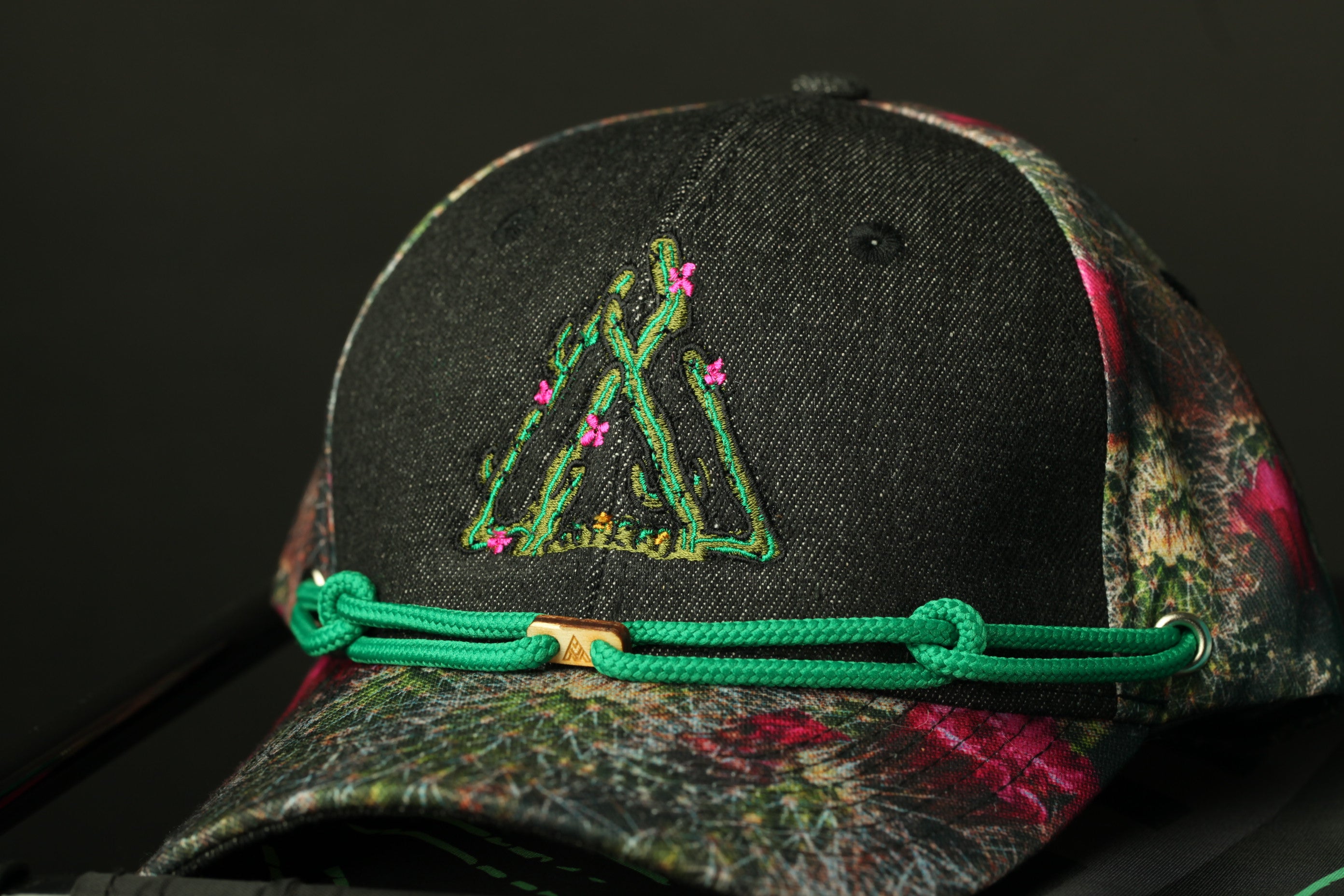 A close-up view of a black baseball cap with a floral pattern and a green string around the brim.