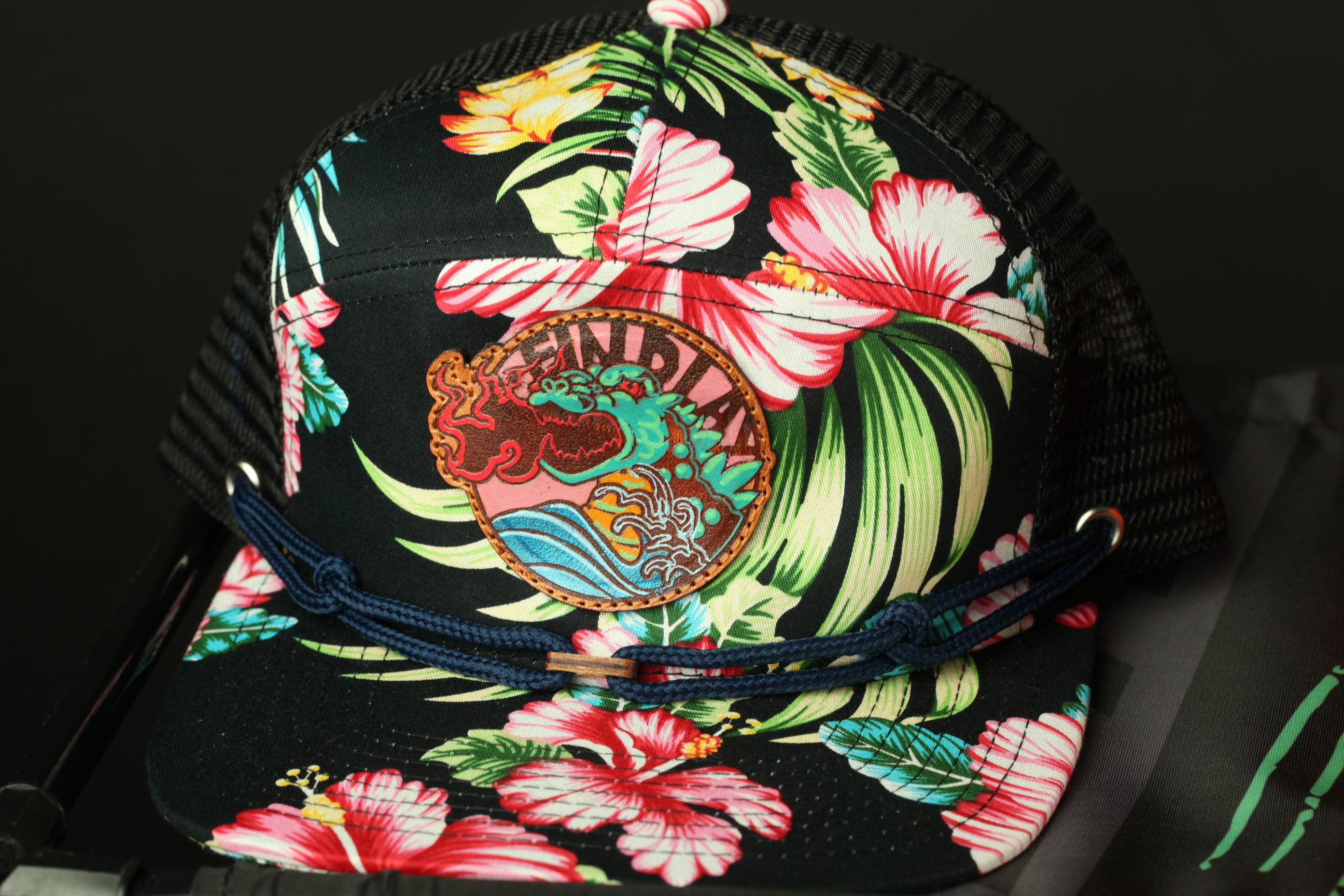 A colorful floral-patterned baseball cap with a tropical design, featuring a large circular logo on the front.