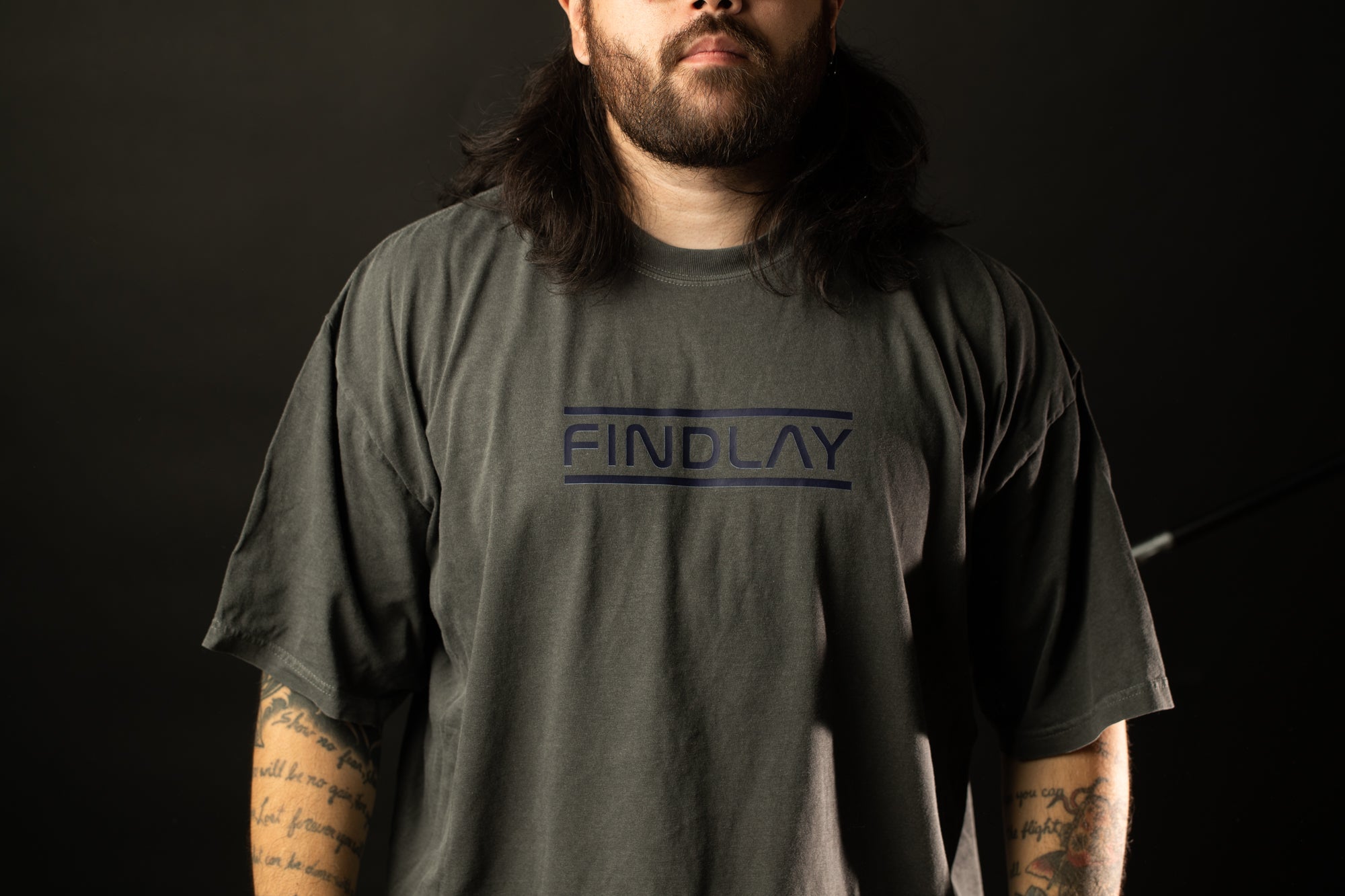 A man with long hair and a beard wearing a gray t-shirt with the text "FINDLAY" printed on it.
