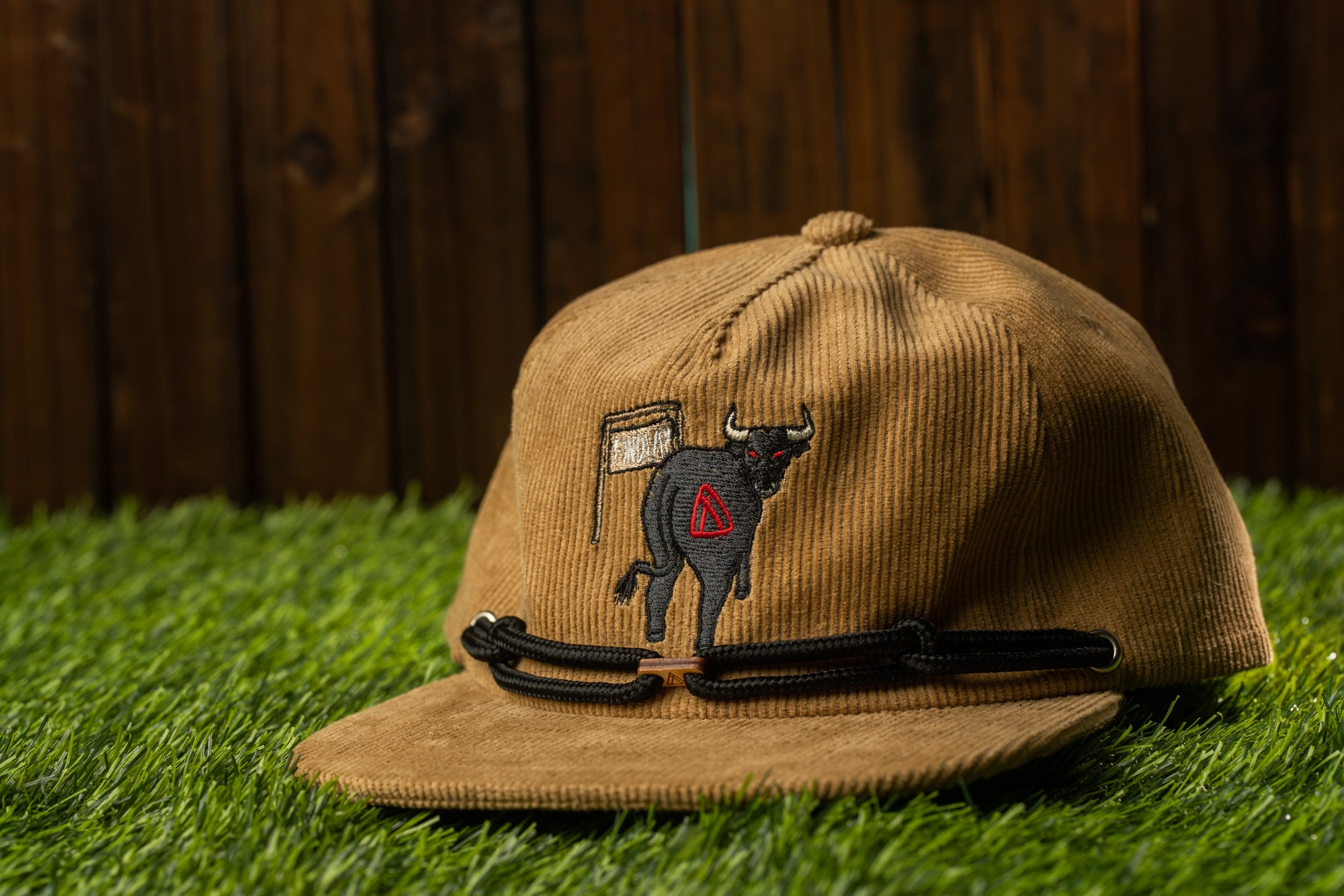 A brown baseball cap with a black bull embroidered on it, placed on a grassy surface.