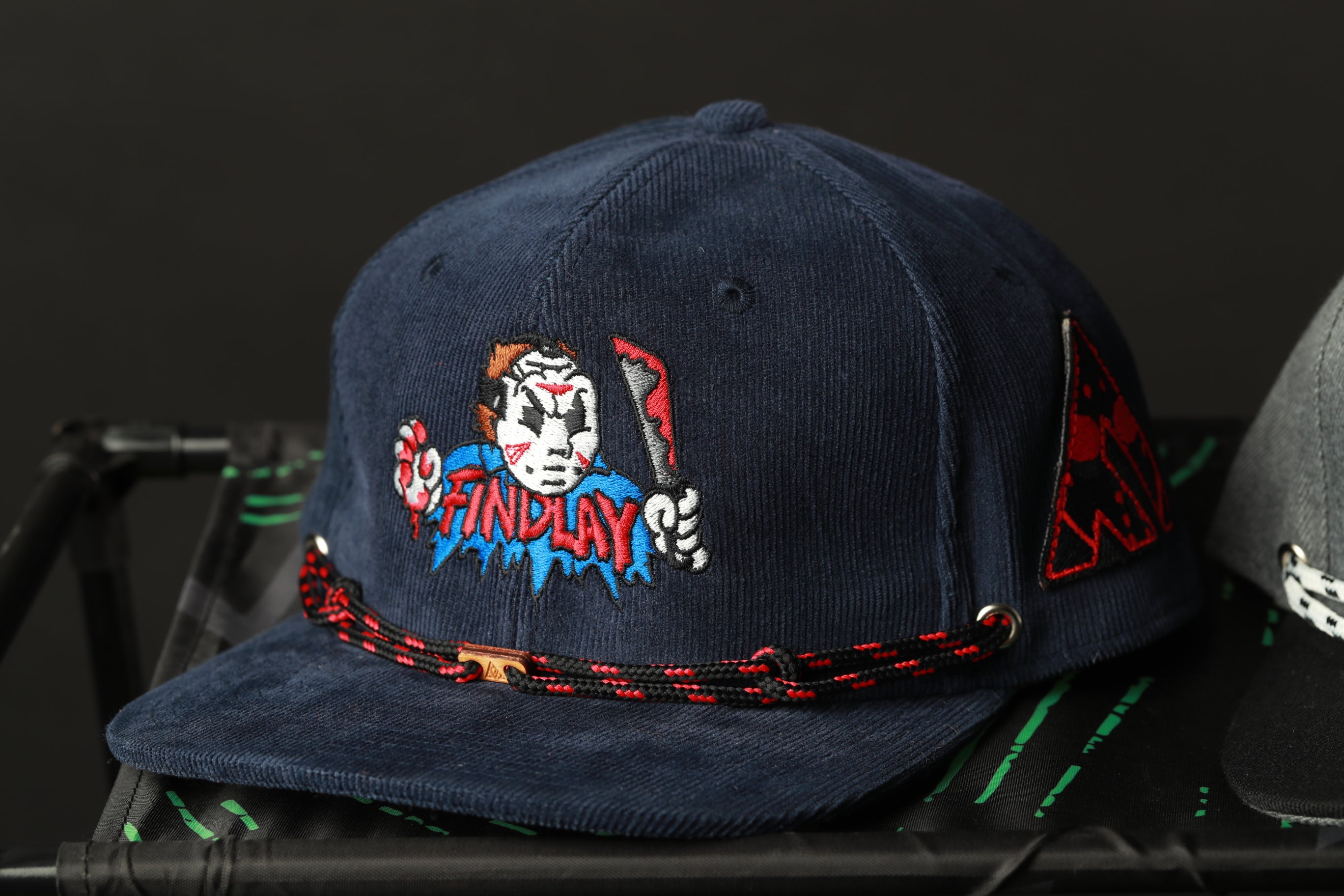 A navy blue baseball cap with a cartoon character and the word "FINDlay" printed on it.