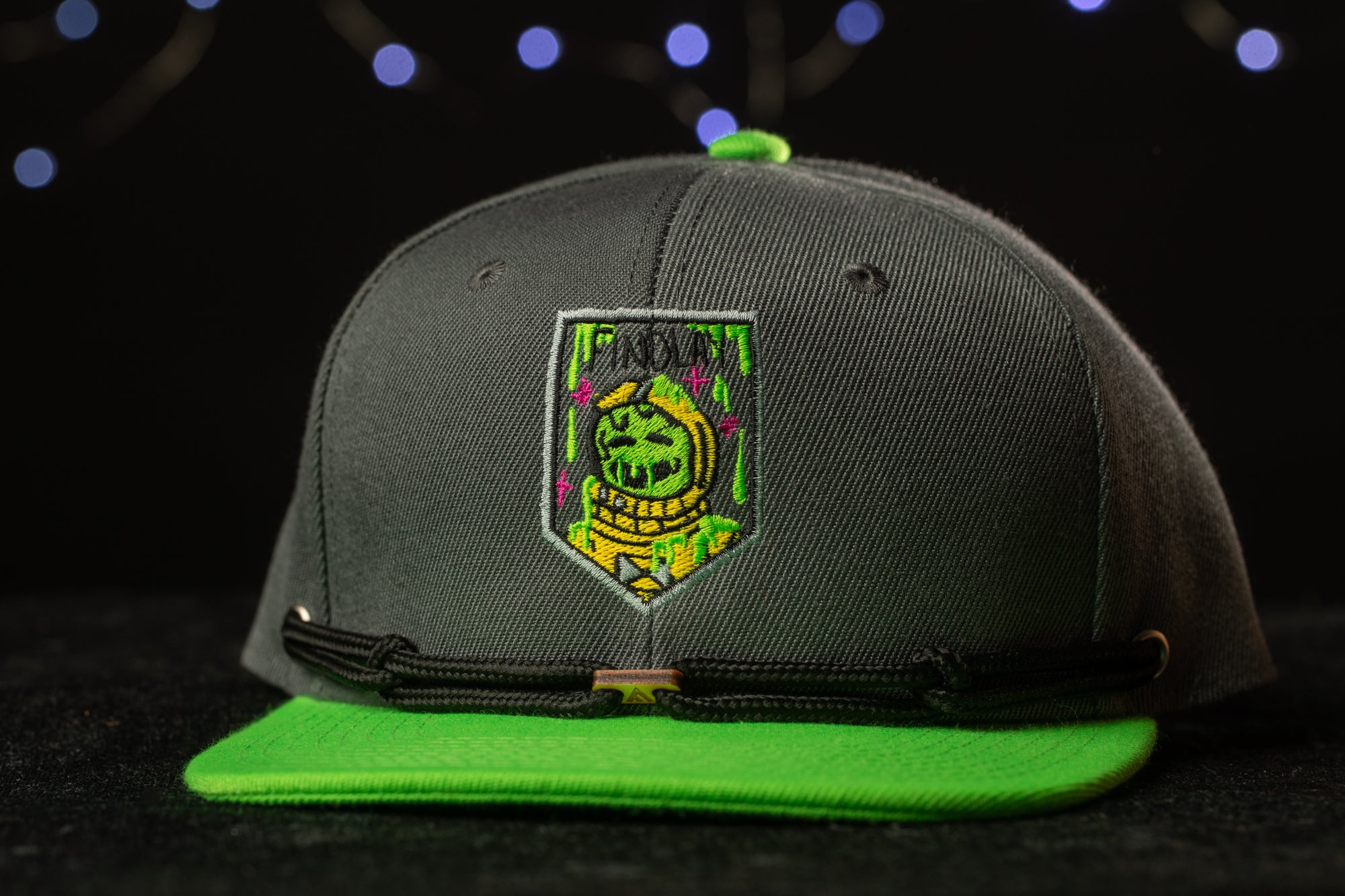 A black baseball cap with a green brim and a patch featuring a green alien character on the front.