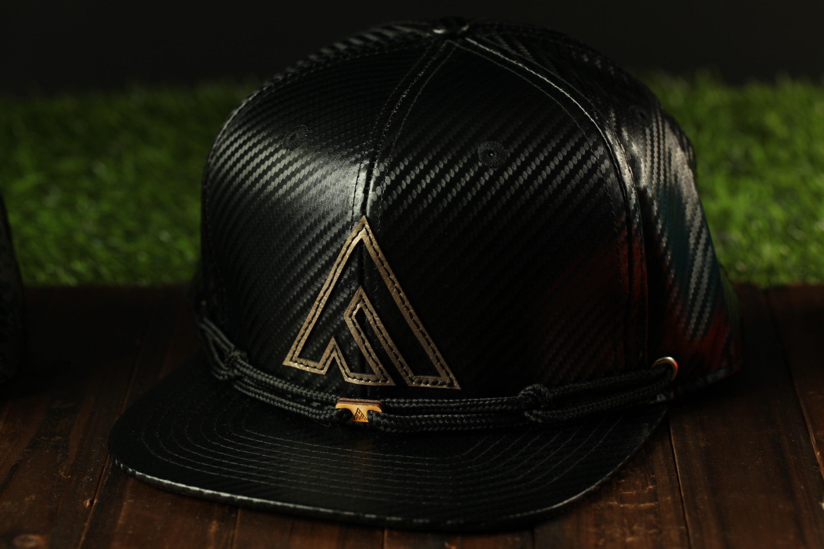 A black baseball cap with a gold logo on the front, placed on a wooden surface.