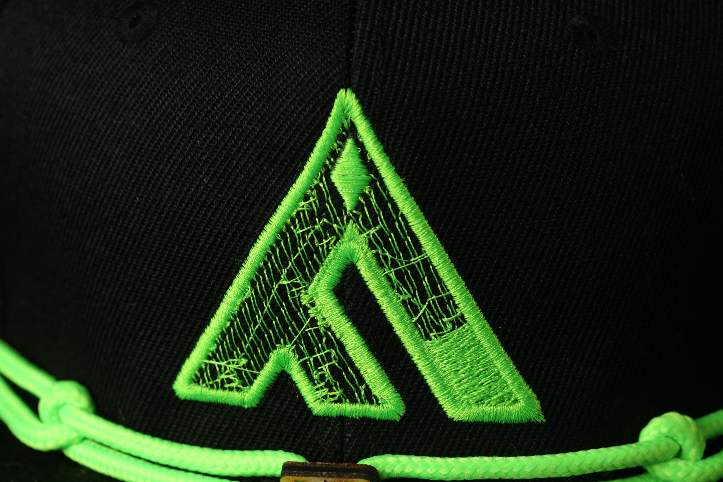 A close-up view of a black baseball cap with a green embroidered logo on the front.