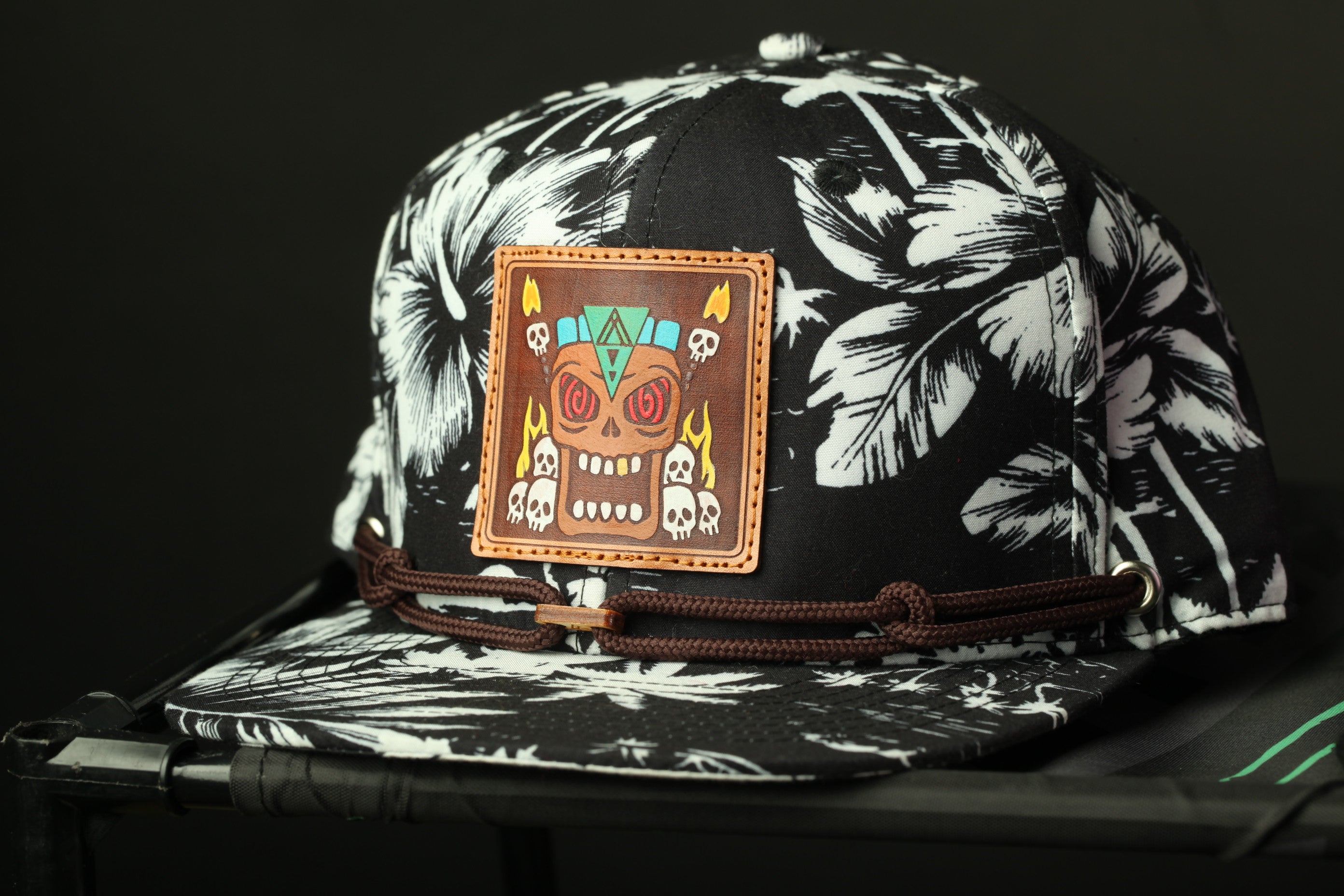 A black and white tropical-themed baseball cap with a colorful skull patch on the front.
