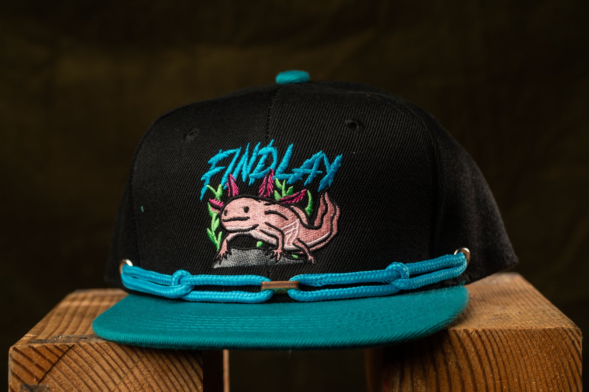 A black baseball cap with a teal brim and a graphic of an axolotl, a type of salamander, on the front.