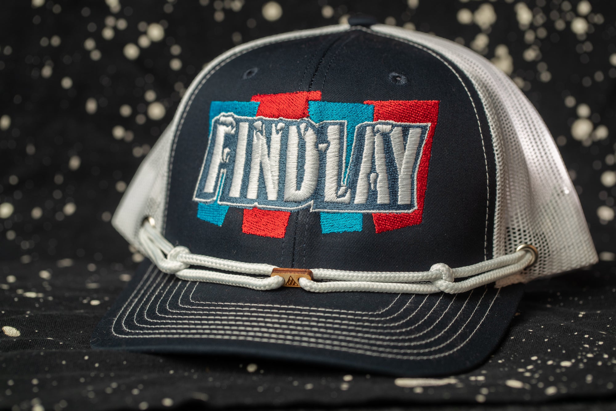 A black baseball cap with a white mesh panel and a white strap, featuring a colorful embroidered logo on the front.