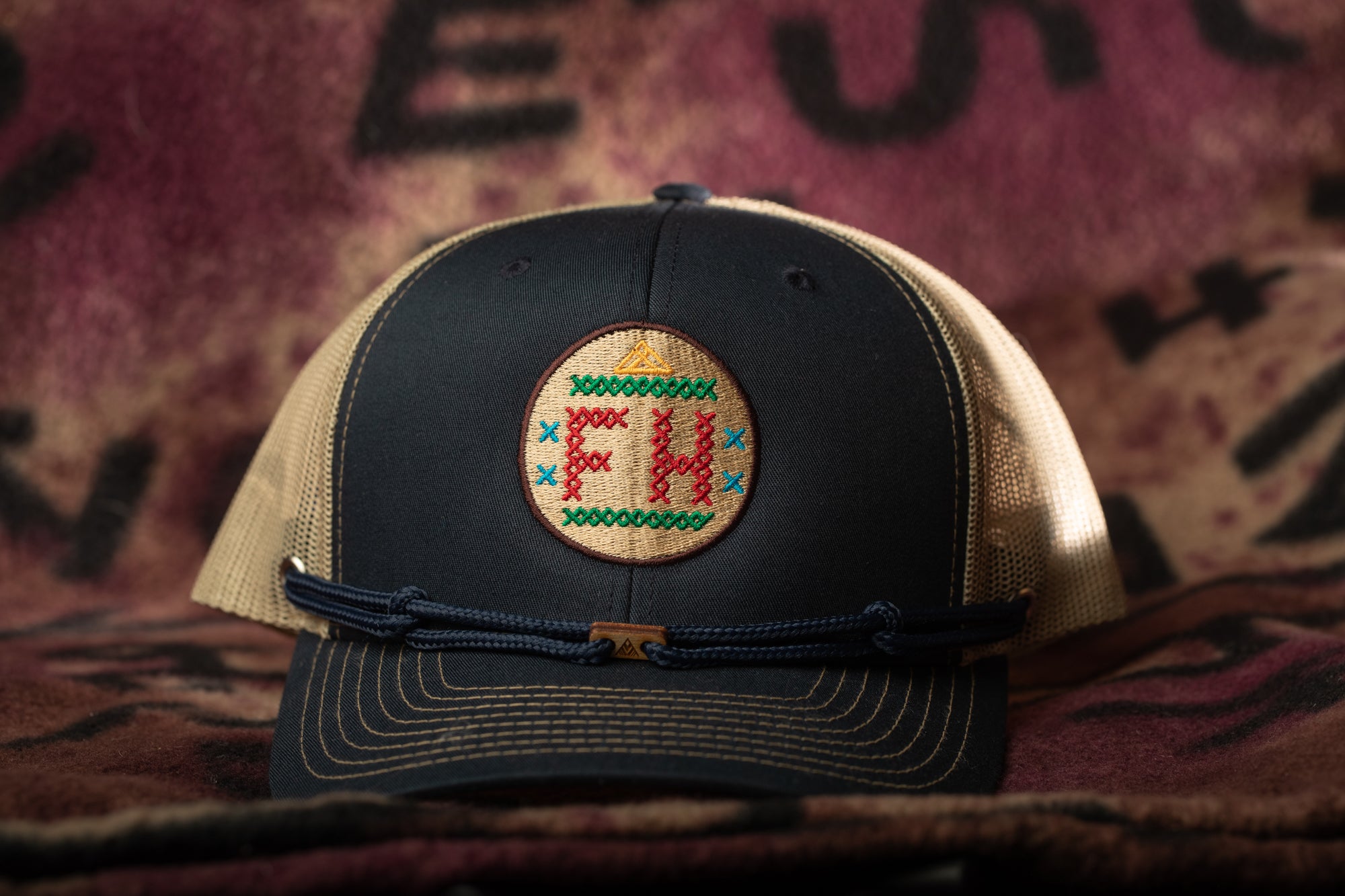 A black baseball cap with a circular patch on the front displaying the letters "FH".