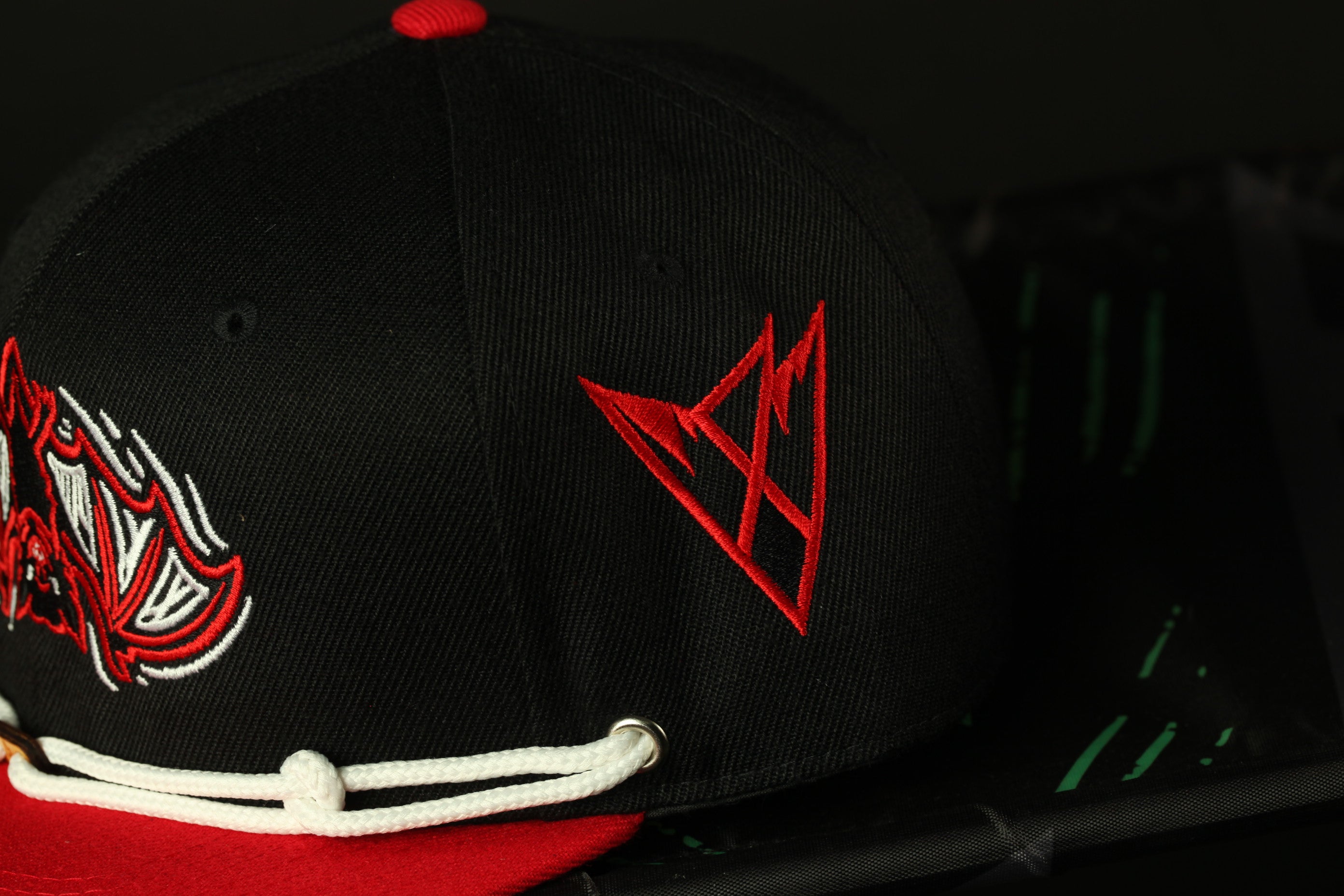 A close-up view of a black baseball cap with red and white embroidered designs, including a red triangle logo on the front.