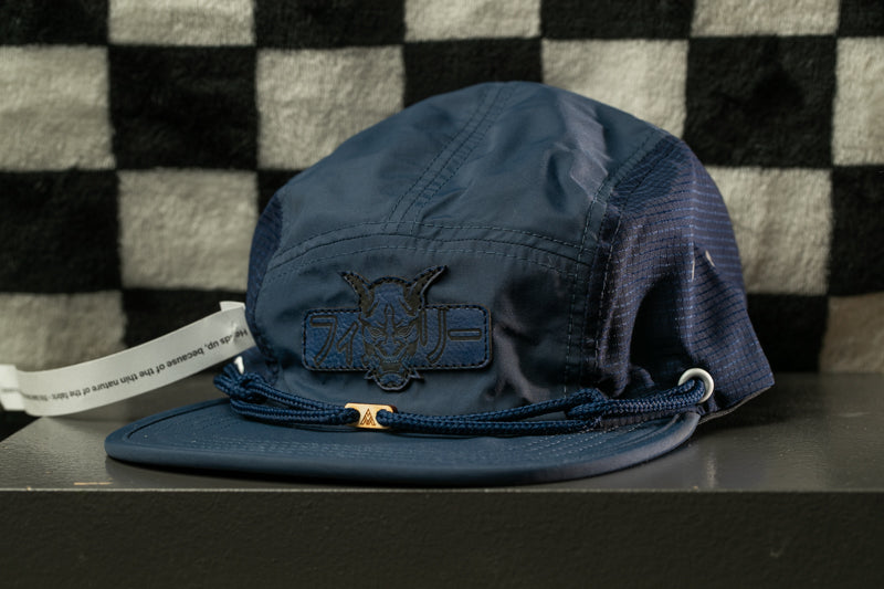 A navy blue baseball cap with a black and white checkered pattern and a small logo on the front, placed on a black surface against a checkered background.