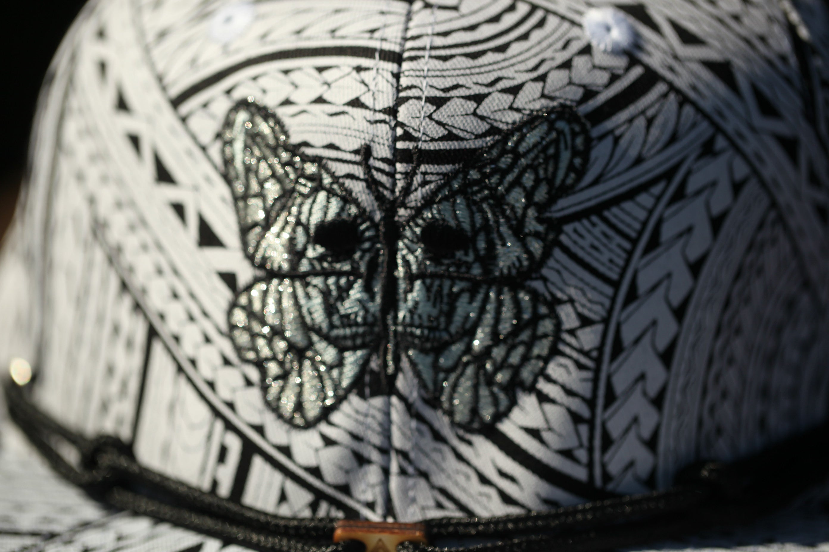 A close-up view of a decorative pattern on a hat, featuring a detailed embroidered design of a butterfly or similar insect.