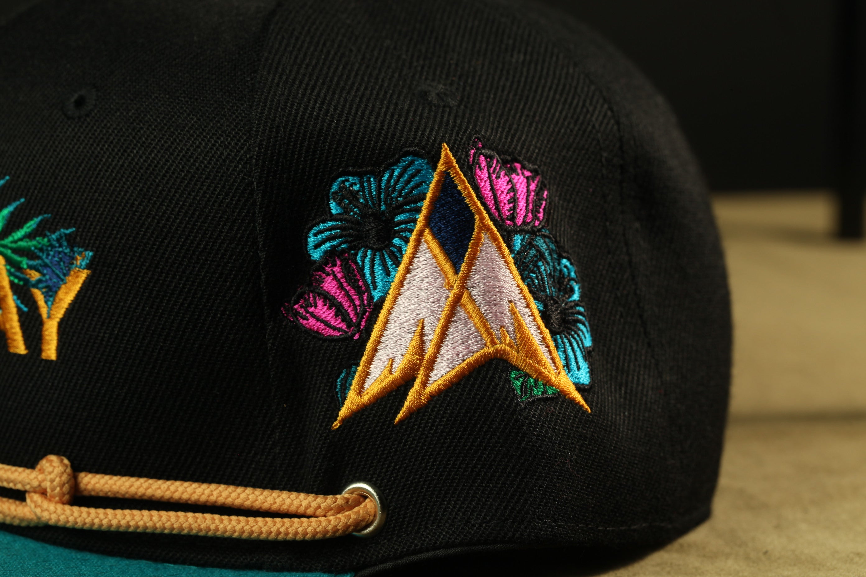 A close-up view of a black baseball cap with colorful floral embroidery on the front.